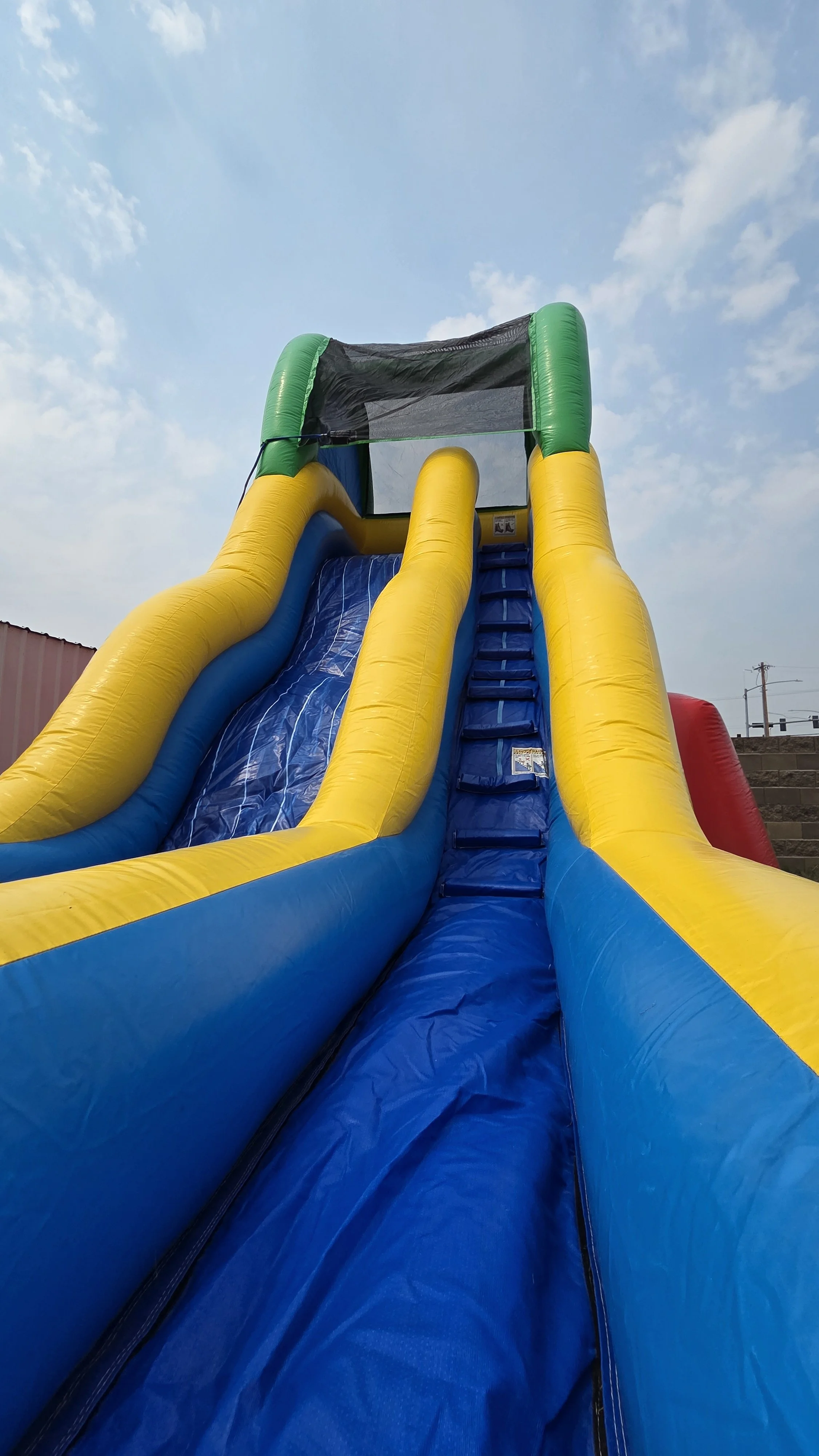Front view of the Flip Flop inflatable waterslide with bright yellow and blue sliding sections beneath a partly cloudy sky.