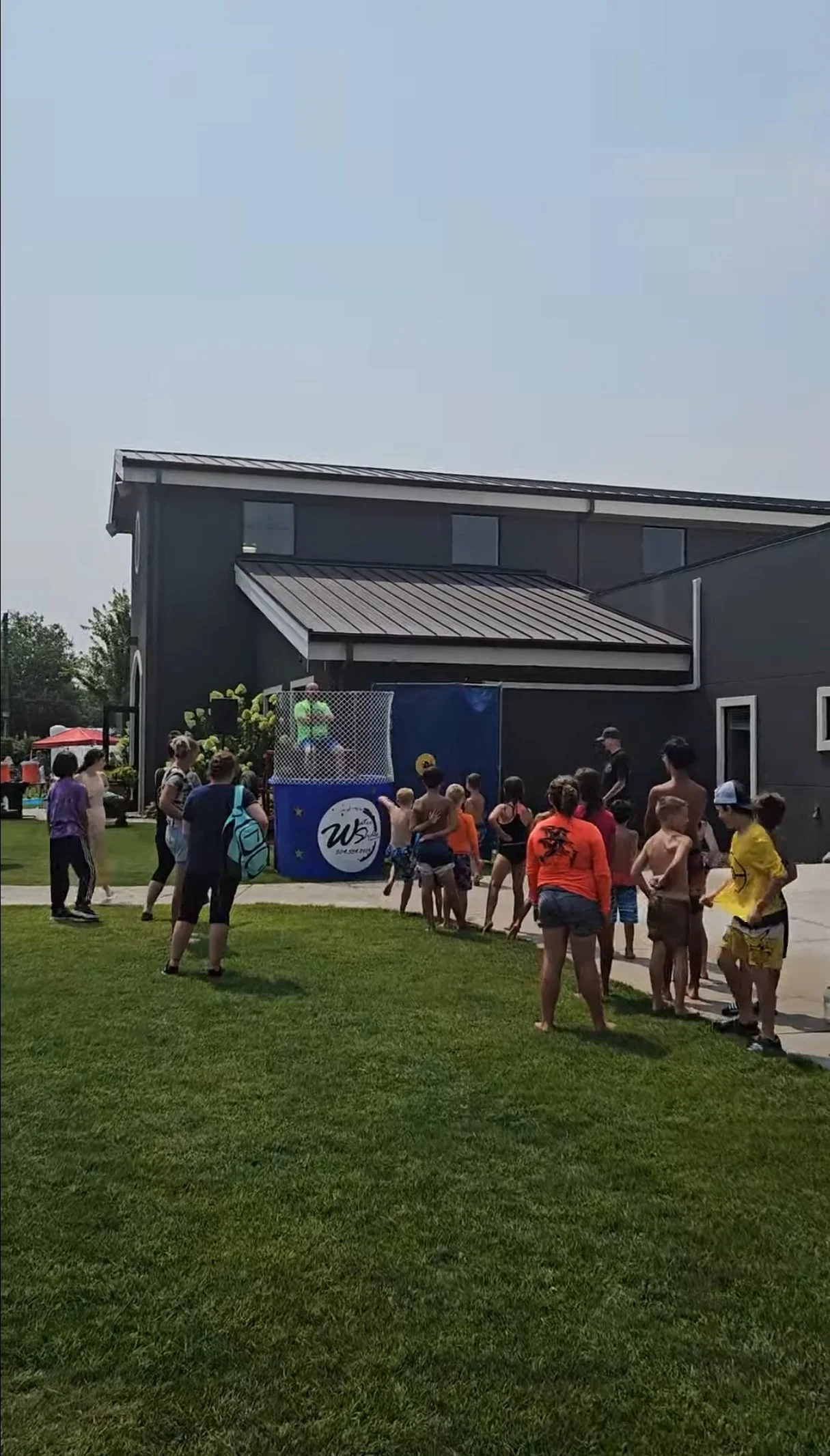 Children and adults gathered outdoors beside the Dunk Dynasty dunk tank during a community event.