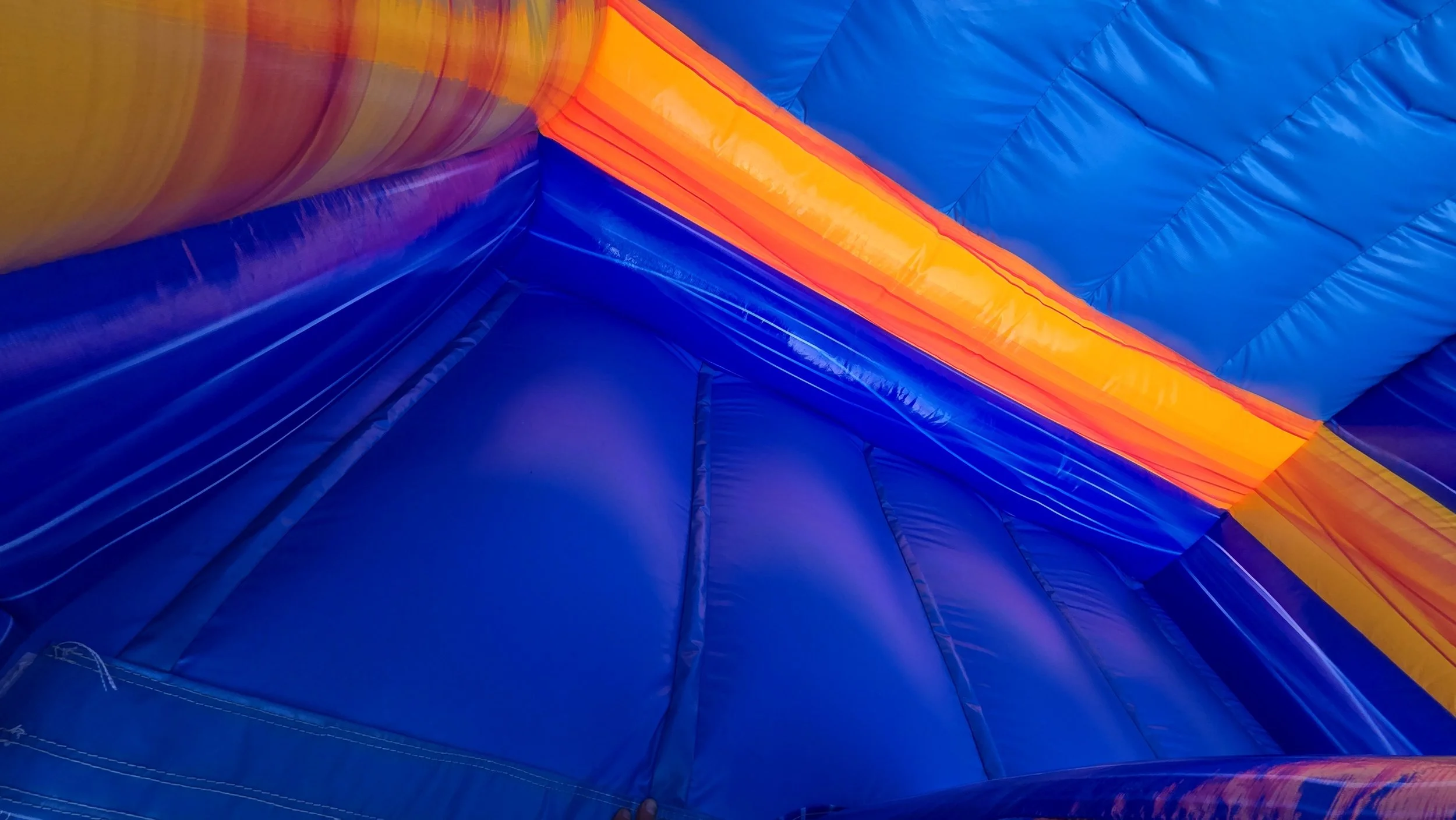 Interior view of the Crazy Coconut inflatable waterslide featuring a blue inflatable floor, colorful walls and protective safety netting.