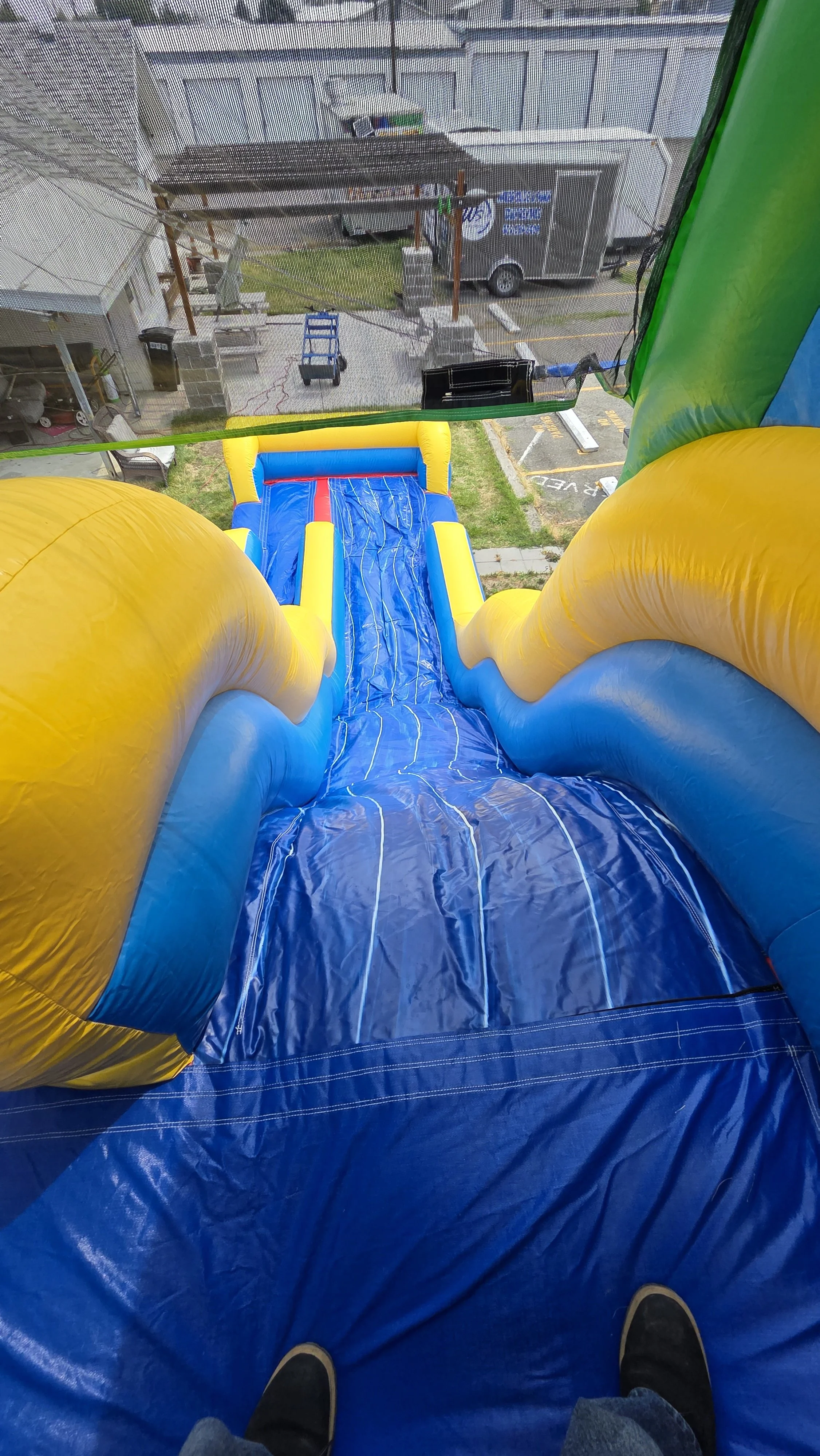 Rider's-eye view down the Flip Flop blue and yellow inflatable waterslide, overlooking the surrounding outdoor area.