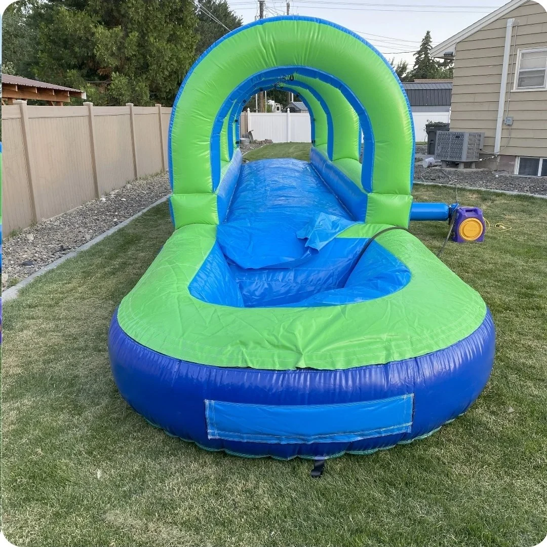 Front view of the Slip Happens inflatable slip-and-slide showing its green arch, blue splash pool and backyard setup.