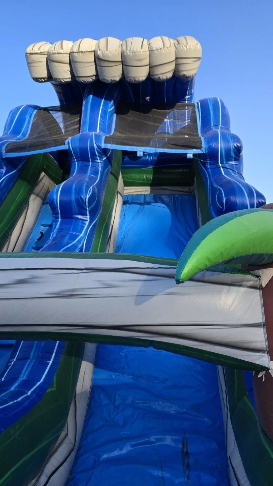 Side view of The Lu'au inflatable waterslide showing its tropical design, tall slide structure and backyard setup.
