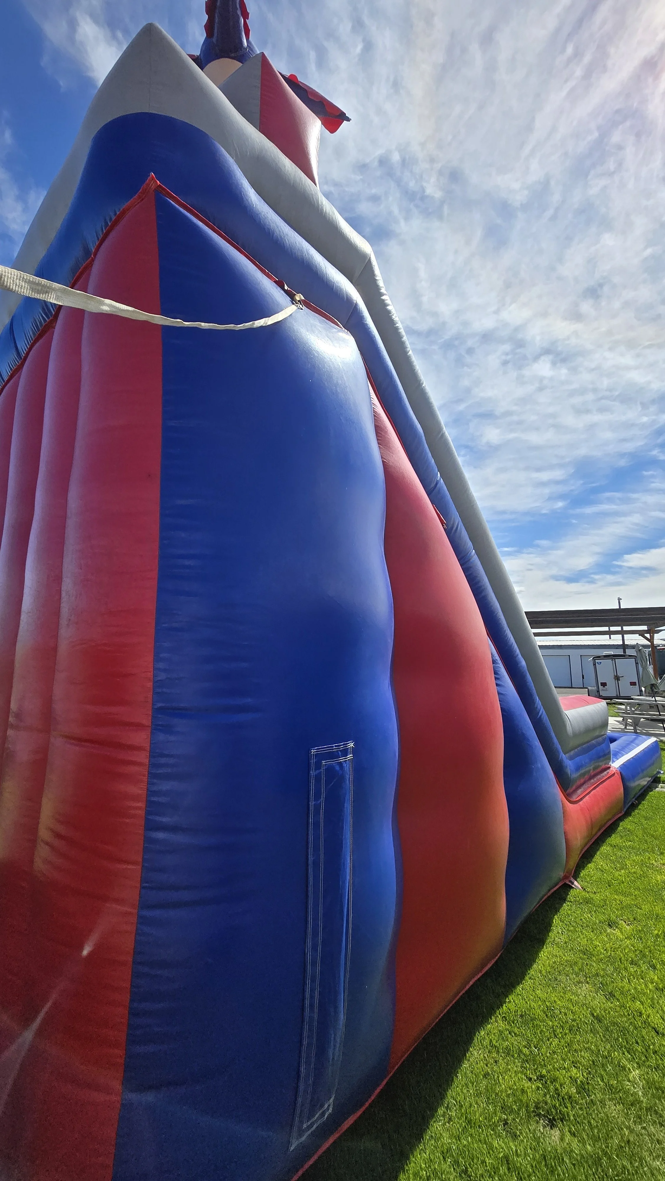 Close-up side view of the tall Red White N' Cool inflatable waterslide showing its red, white and blue exterior beneath a partly cloudy sky.
