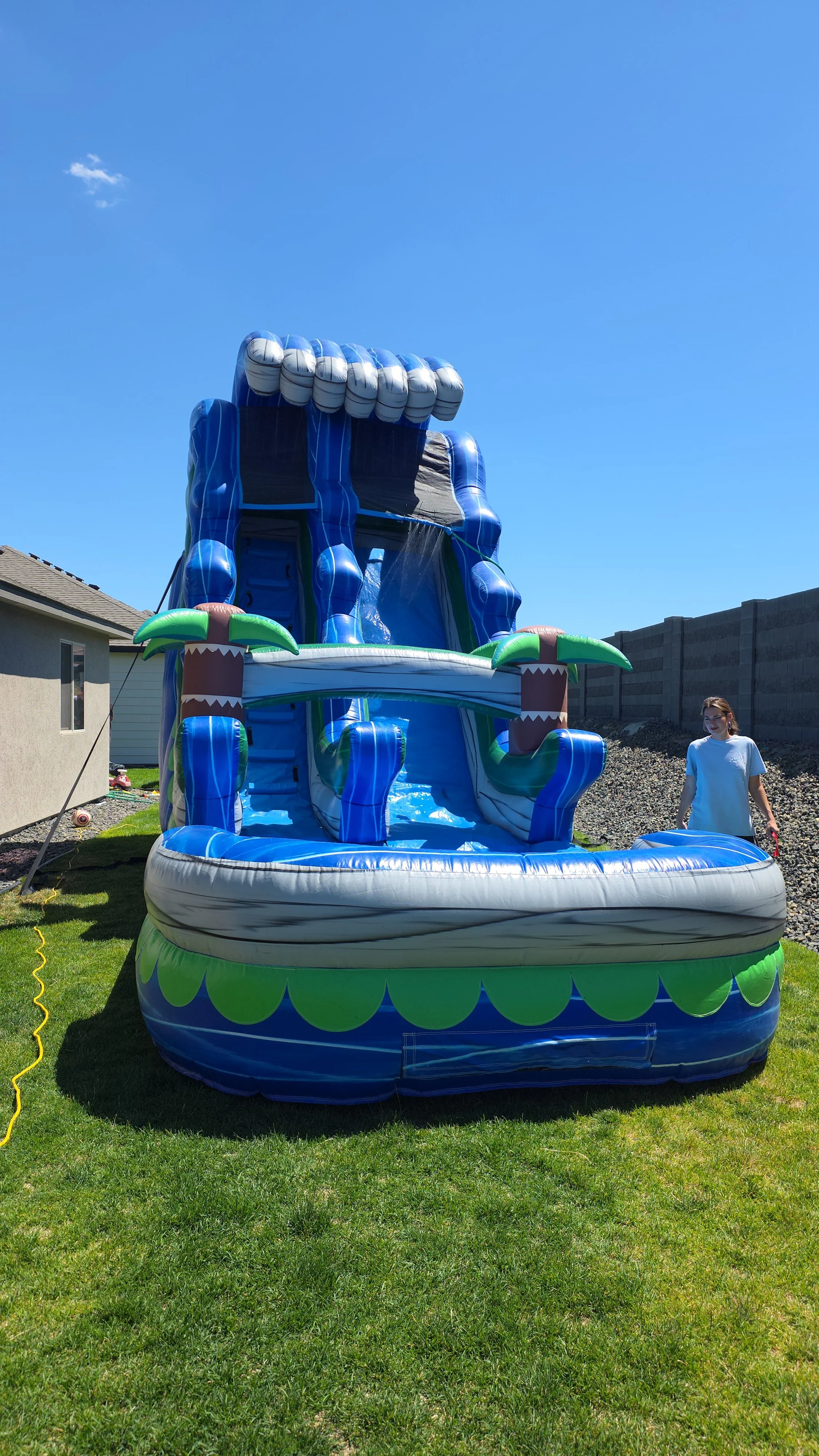 Front view of The Lu'au tropical inflatable waterslide with bright blue and green colors, palm-tree decorations and a large splash pool.