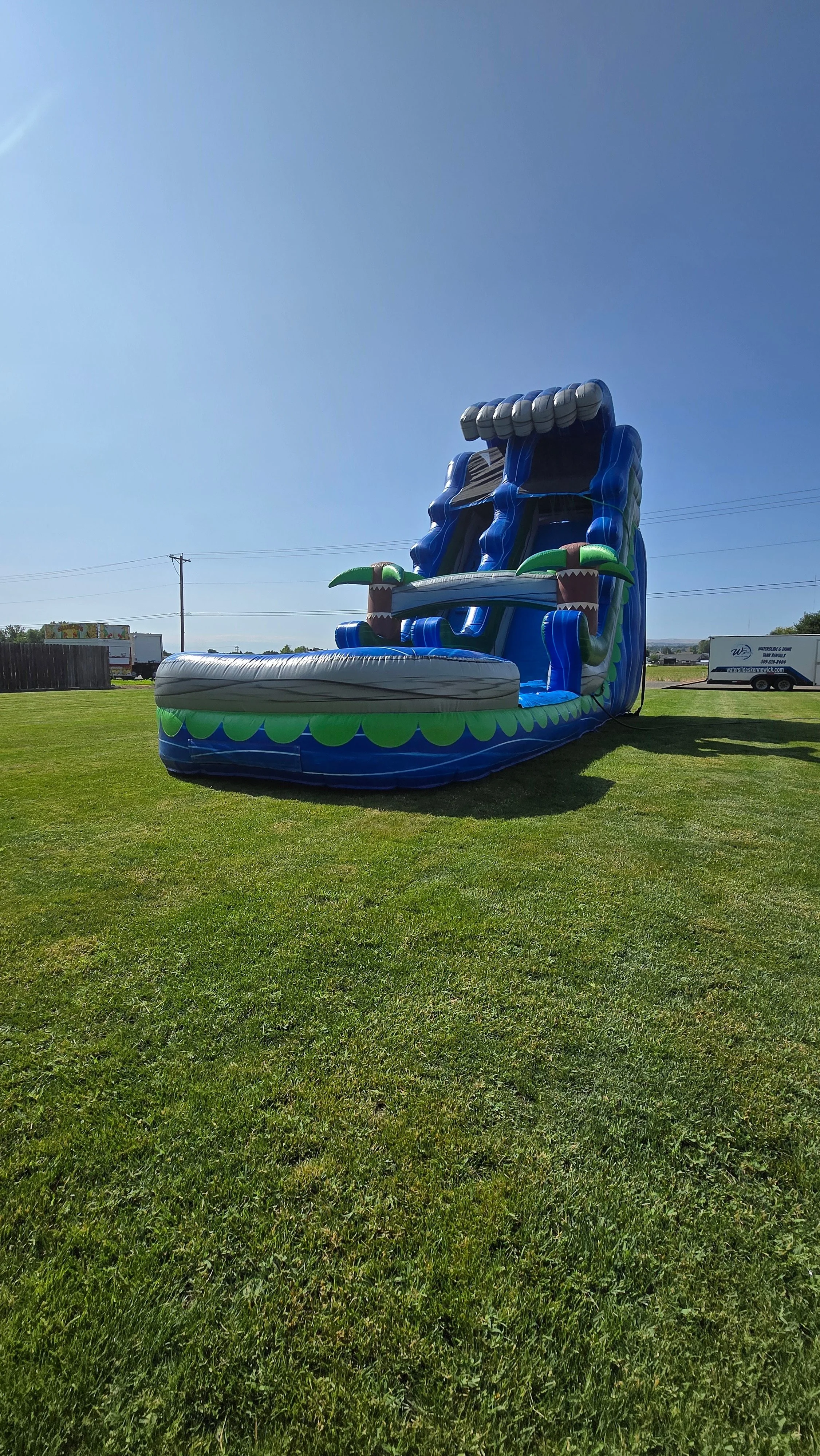 Front view of The Lu'au tropical inflatable waterslide with bright blue and green colors, palm-tree decorations and a large splash pool.