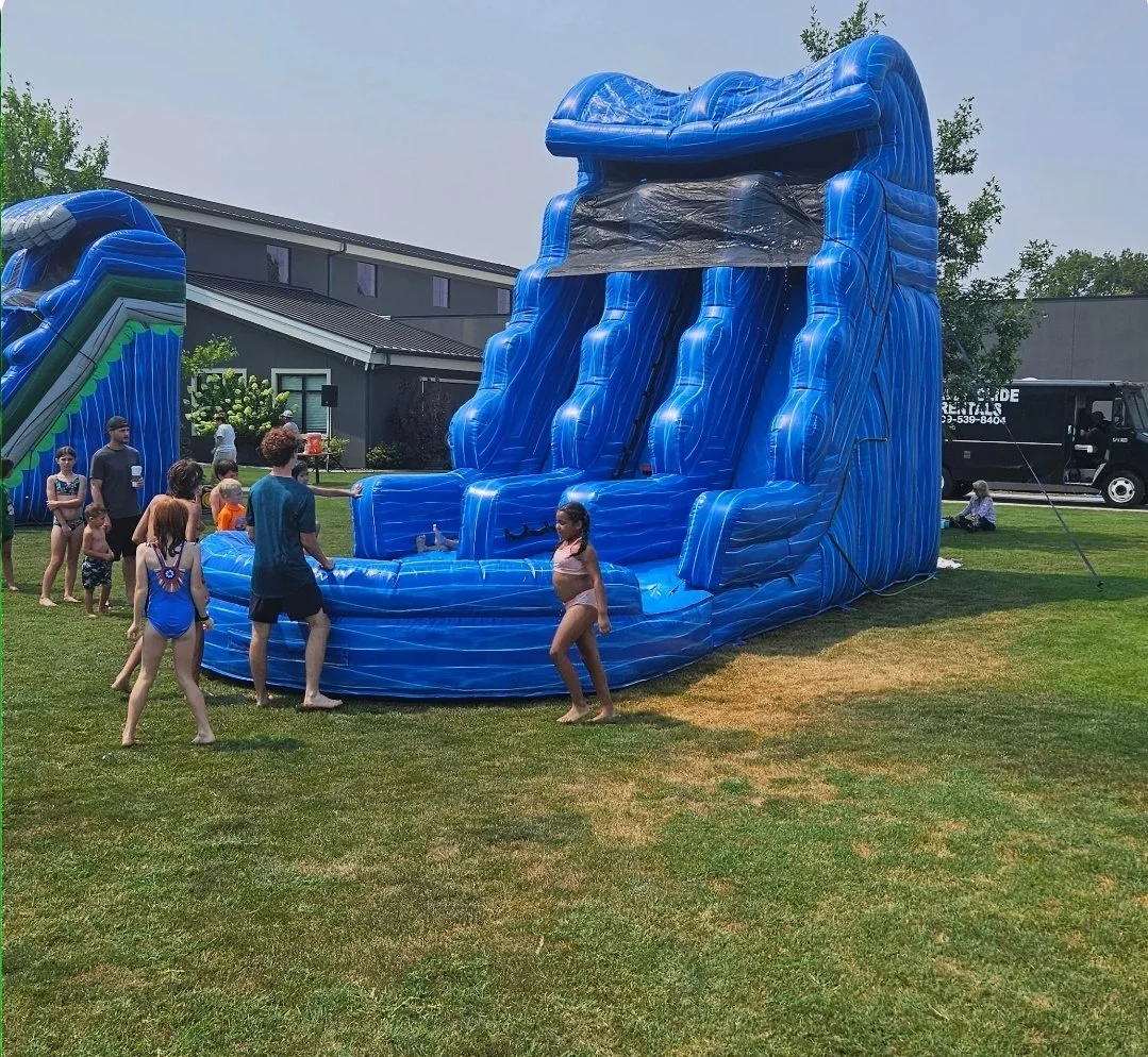 Double Trouble dual-lane inflatable waterslide set up outdoors on a grassy lawn, showing its towering blue structure and large splash pool during an event.