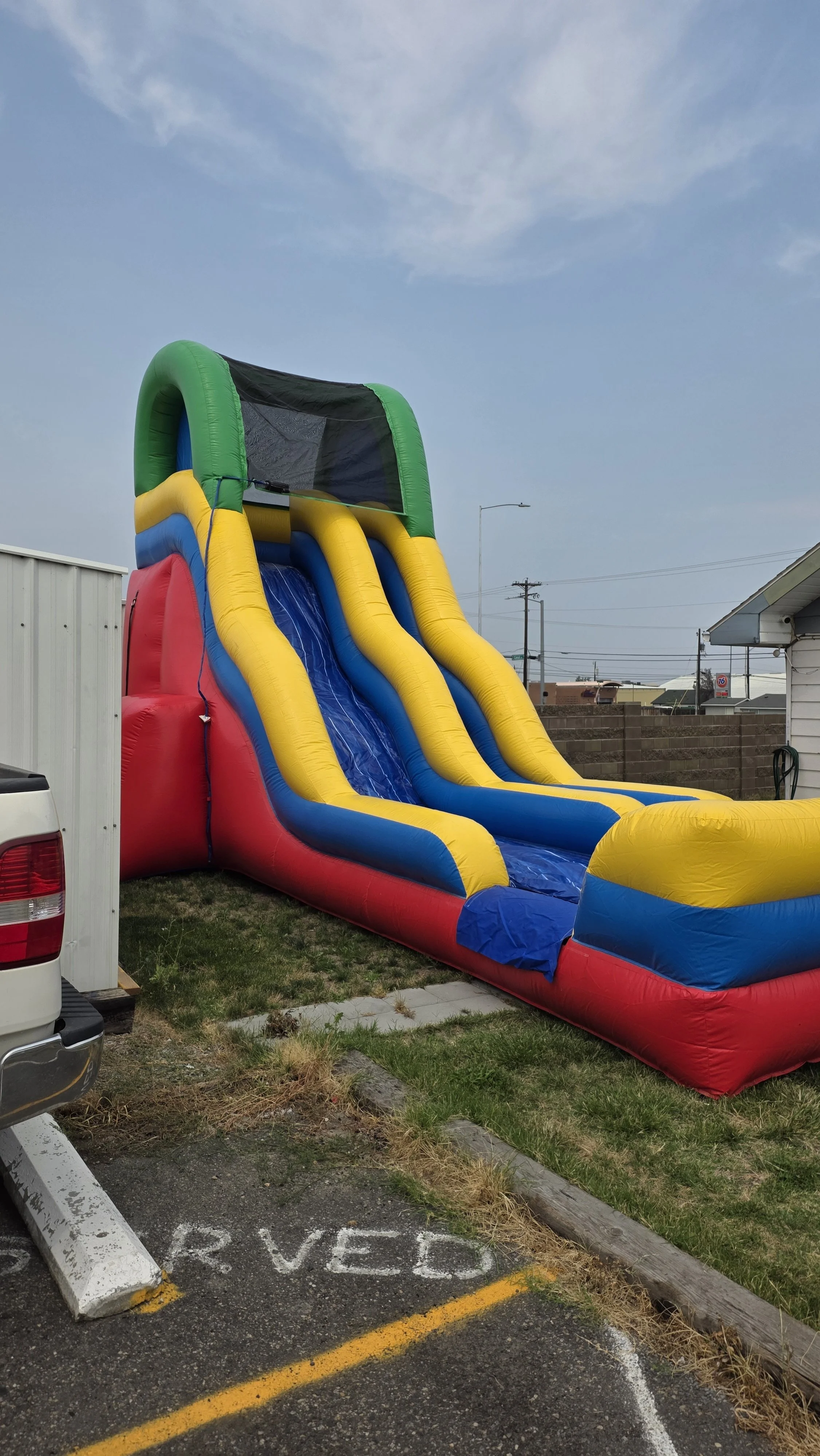View from the top of the Flip Flop inflatable waterslide, looking down its blue sliding lane between bright yellow inflatable sides.