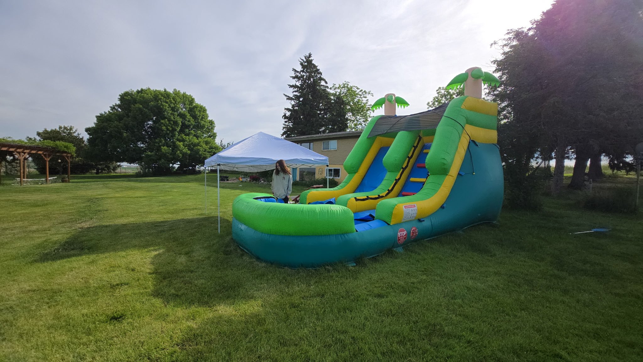 Wide side view of The Tiki tropical inflatable waterslide set up in a spacious grassy yard for an outdoor summer event.