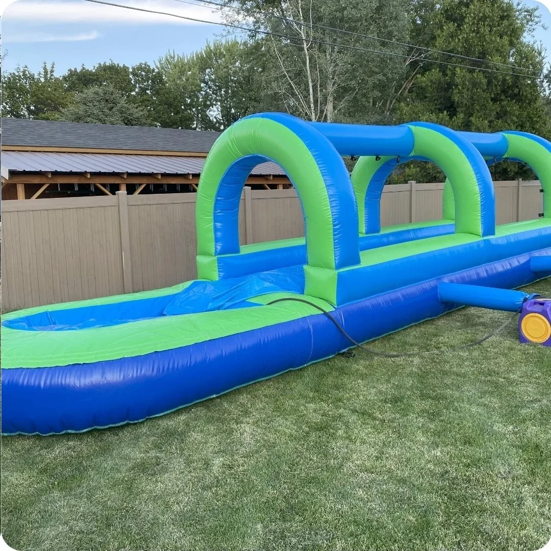 Full-length side view of the Slip Happens green and blue inflatable slip-and-slide set up on grass for summer parties in the Tri-Cities.