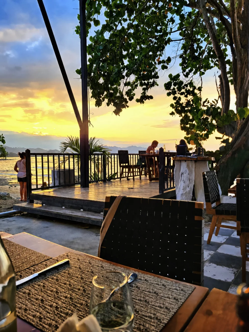 Sunset over the sea from an open-air deck shaded by palm trees