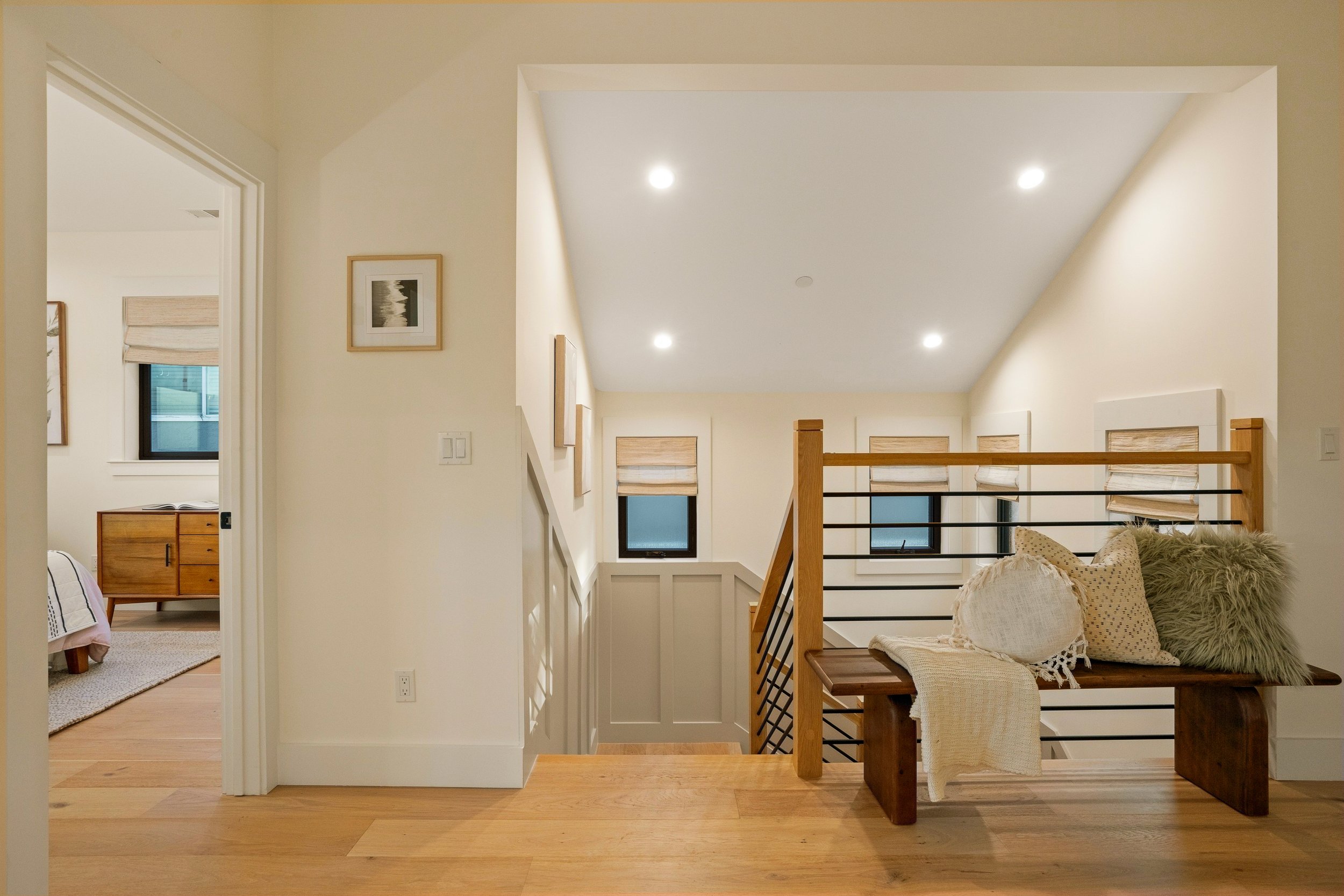 Interior view of a modern home with a staircase, beige walls, hardwood floors, and a seating area with pillows.