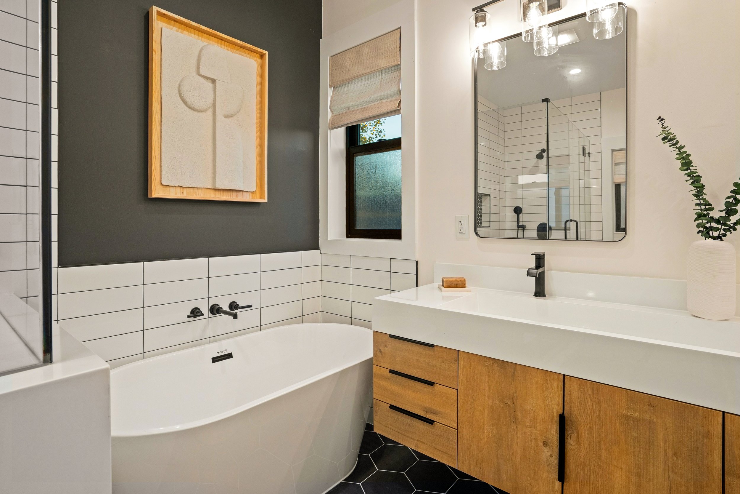 Modern bathroom with white tile walls, black fixtures, wooden vanity, large mirror, and a bathtub.