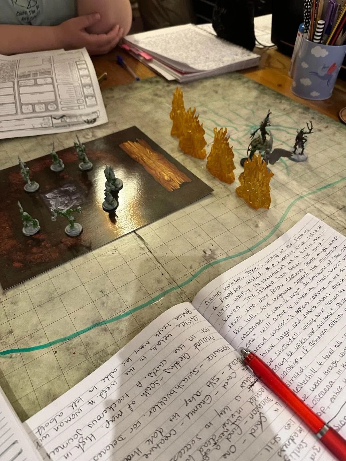 Tabletop role-playing game setup with miniature figures, a map, a notebook with handwritten notes, and gaming accessories.