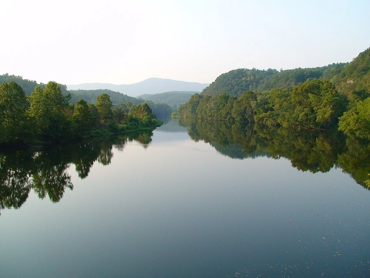 Calm river reflecting lush forested hills and distant mountains