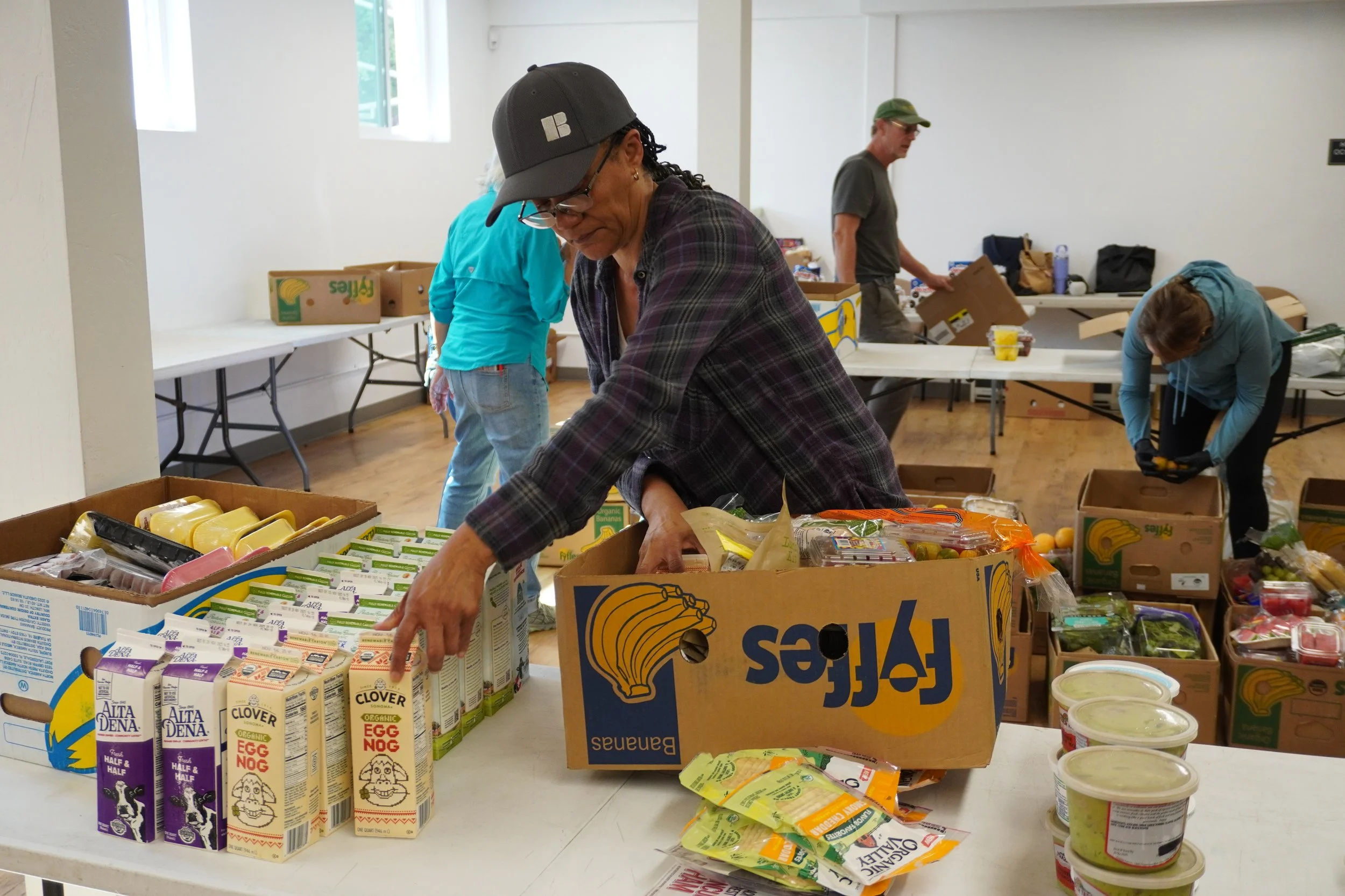 Volunteers sort fresh produce, dairy, and groceries into boxes at a community food distribution center.