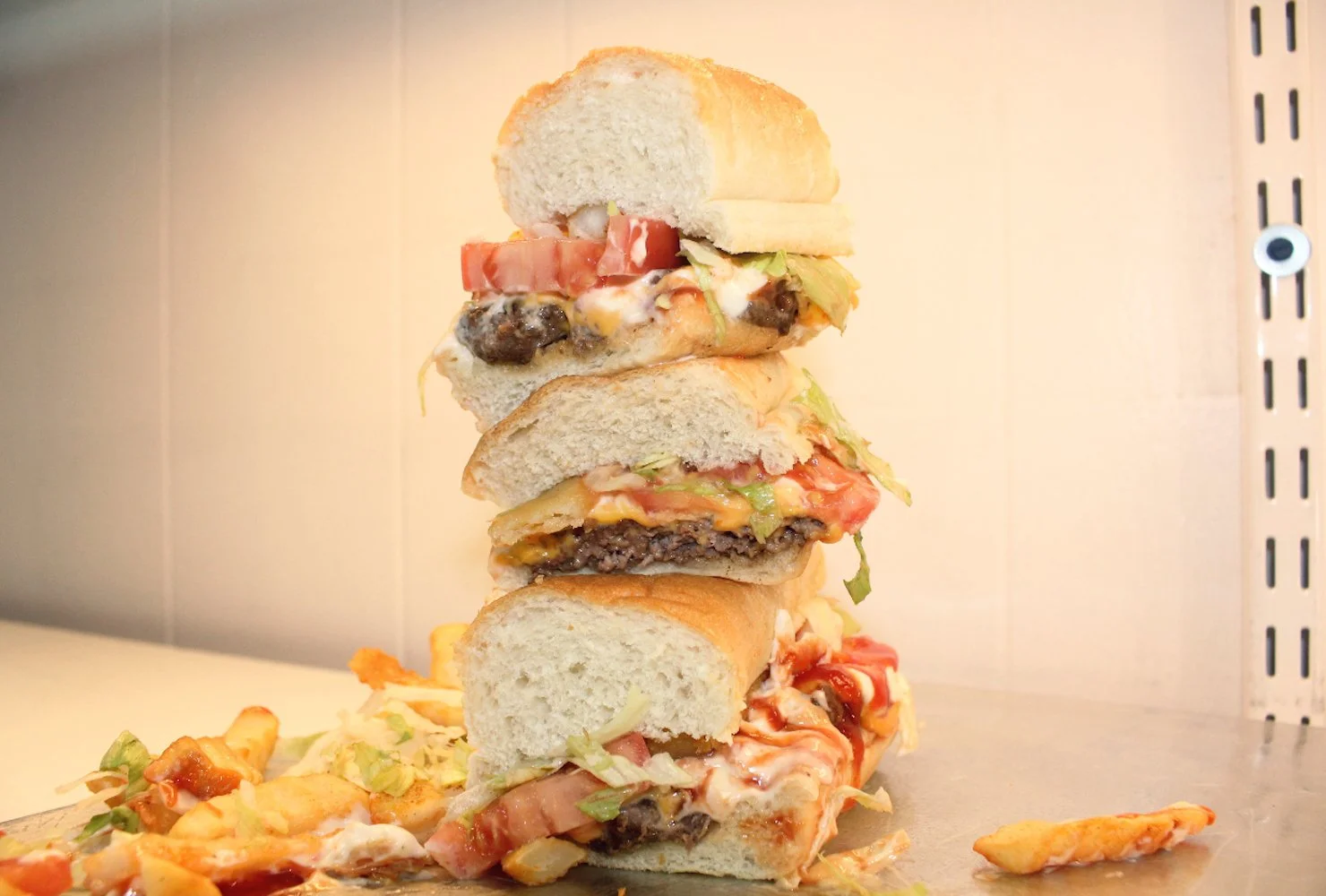 Stacked cheeseburgers with buns, lettuce, tomato, cheese, hamburger patty, and toppings, with some food mess on the surface