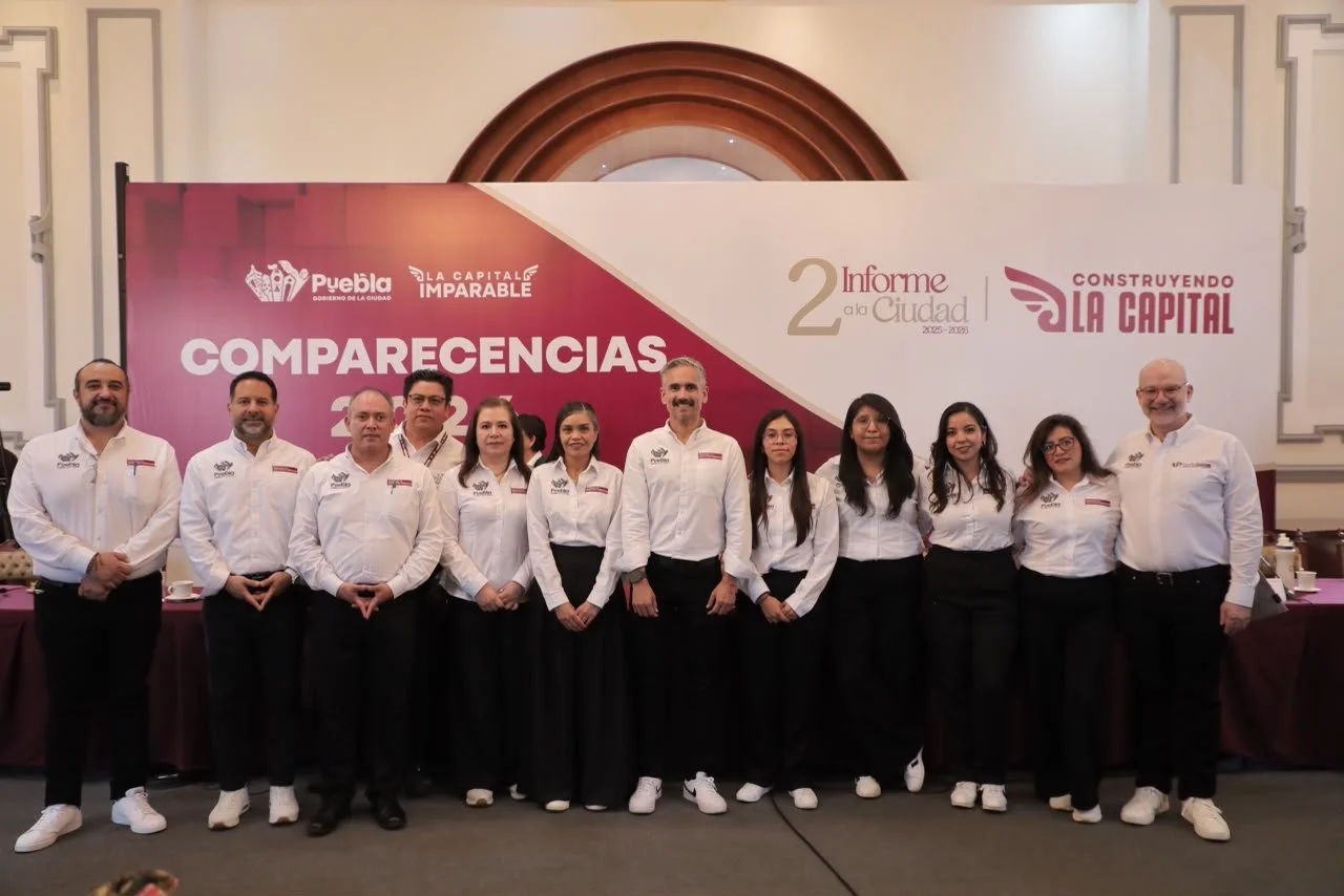 Grupo de personas en una conferencia, vista frontal, con póster de fondo que dice 'COMPARECENCIAS 2023' y logos del gobierno de Puebla y del informe a la ciudad 2023-2028.