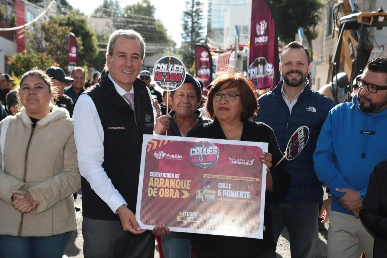 Grupo de personas en una ceremonia de inicio de obra en la calle 6 Poniente, con pancartas y señalización, en una calle de una ciudad.