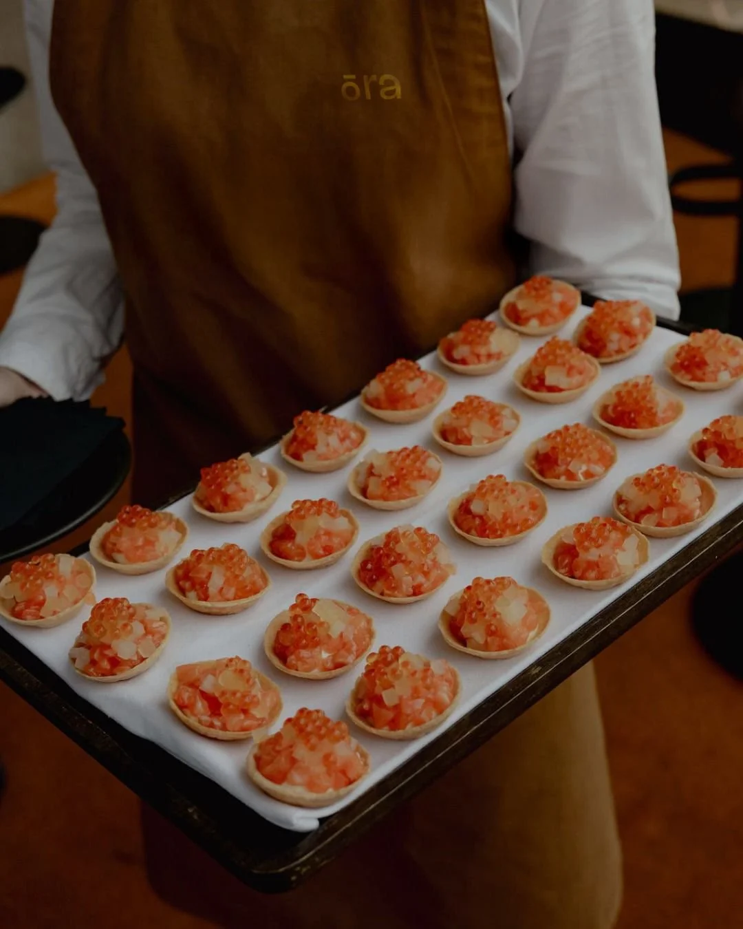 Server holding a tray of bite-sized savory tartlets topped with shrimp and orange fish roe