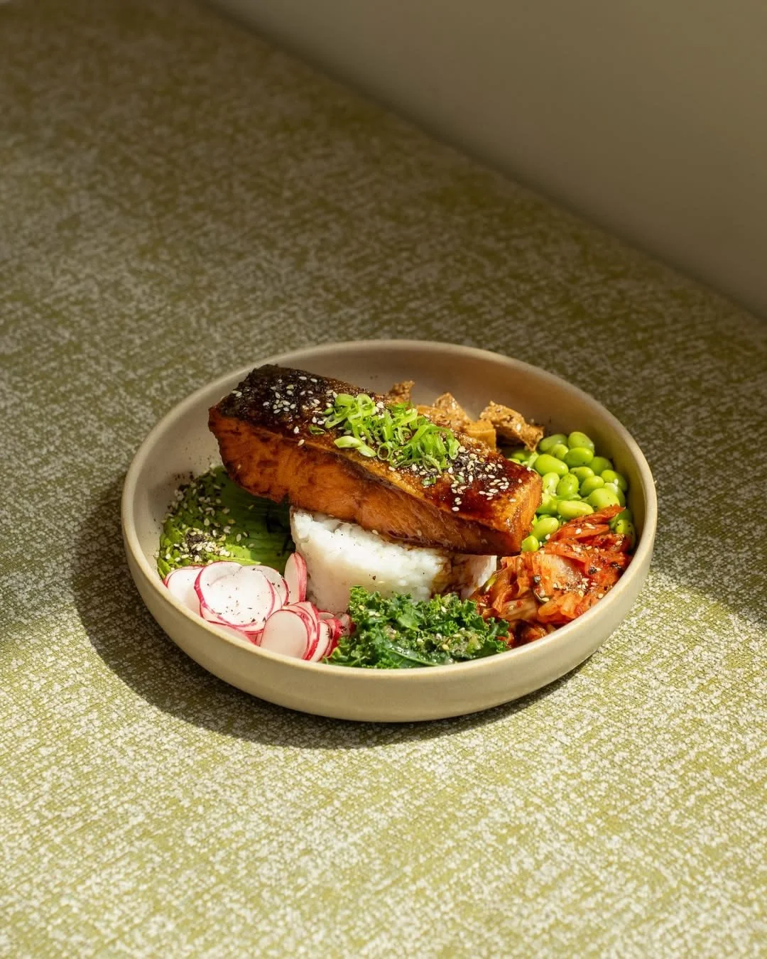Glazed sesame-crusted salmon rice bowl with edamame, kimchi, radishes, greens, and scallions