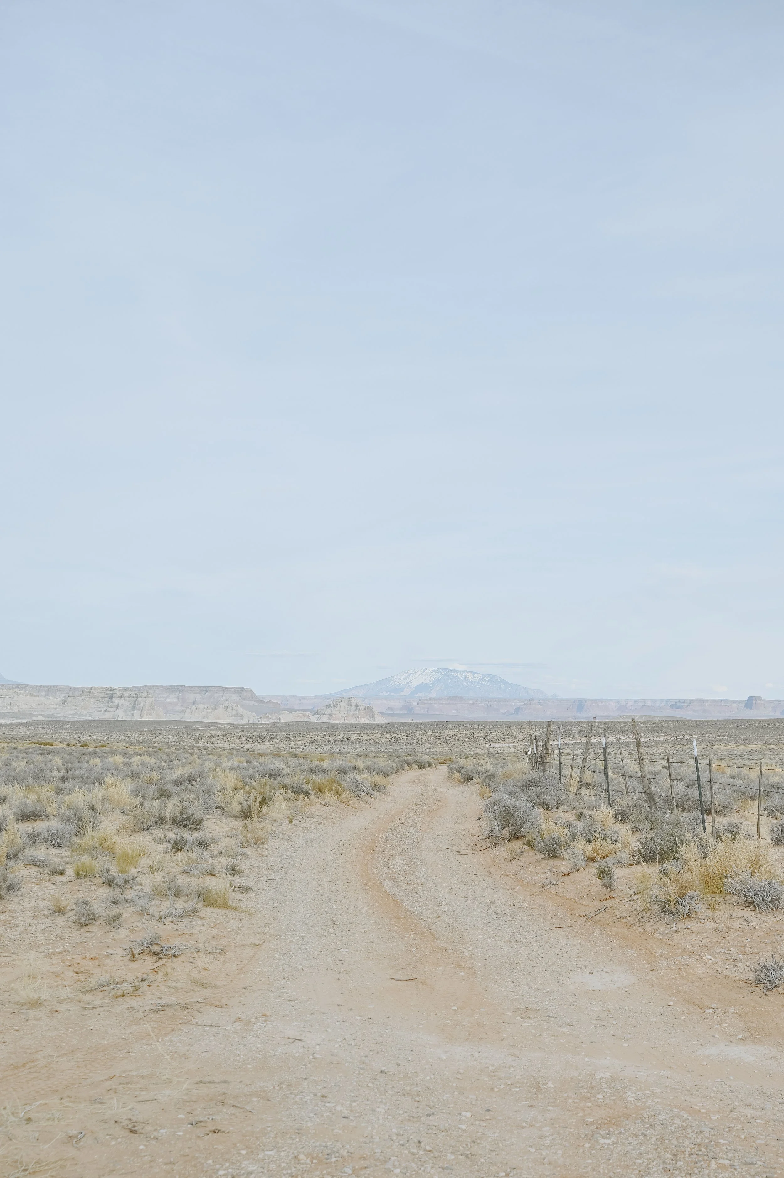 Dirt track winding across pale desert toward a distant mesa under a cloudy sky.