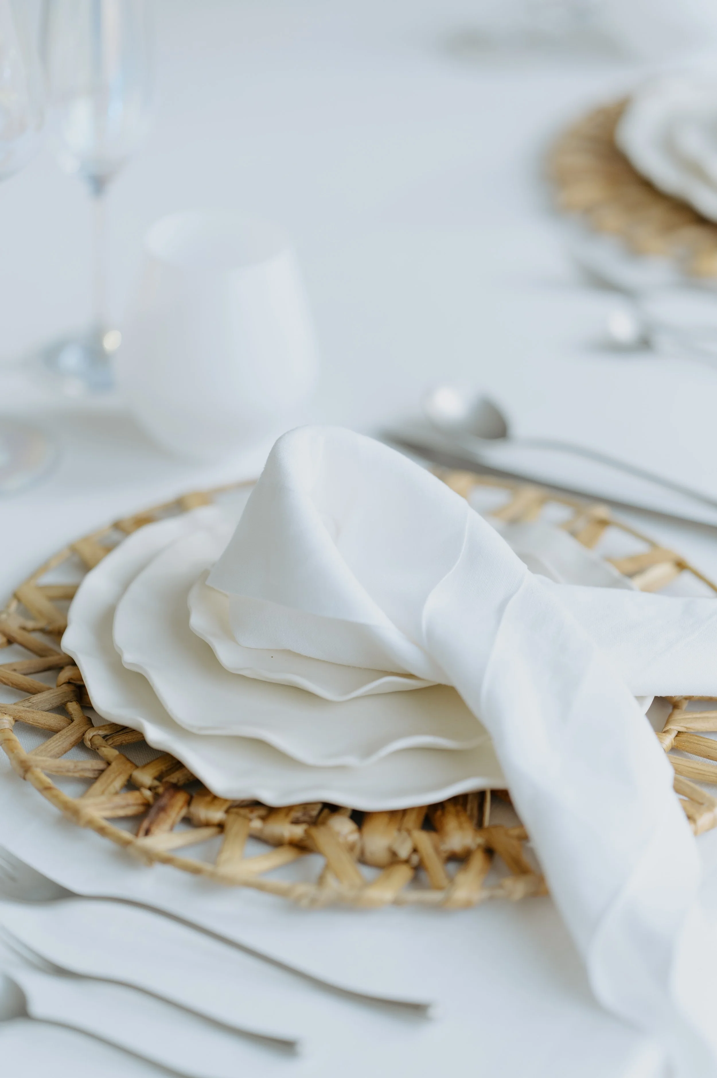 A folded linen napkin on a white plate with a woven charger.
