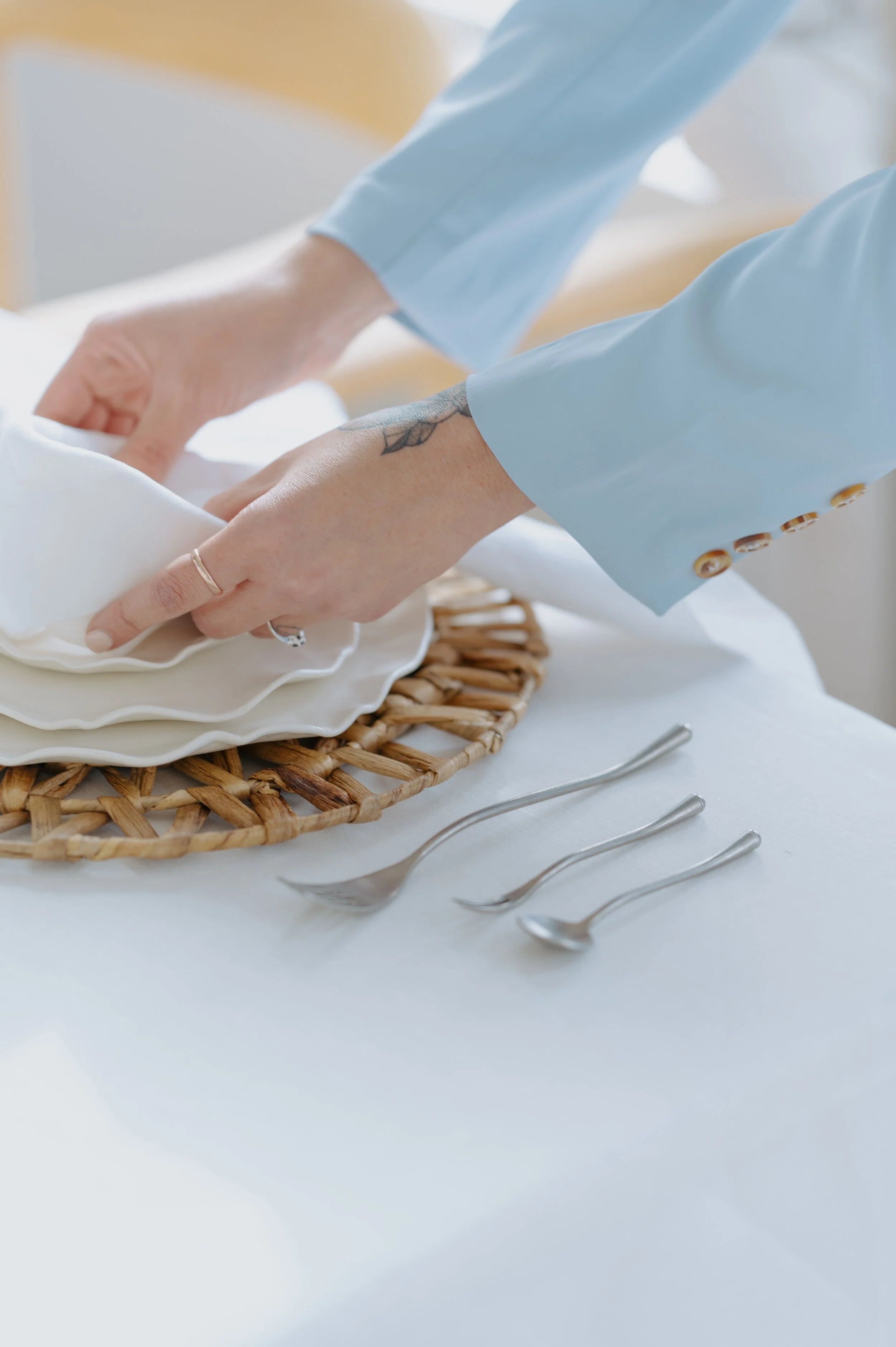 Hands setting a napkin on a white plate with silver flatware.
