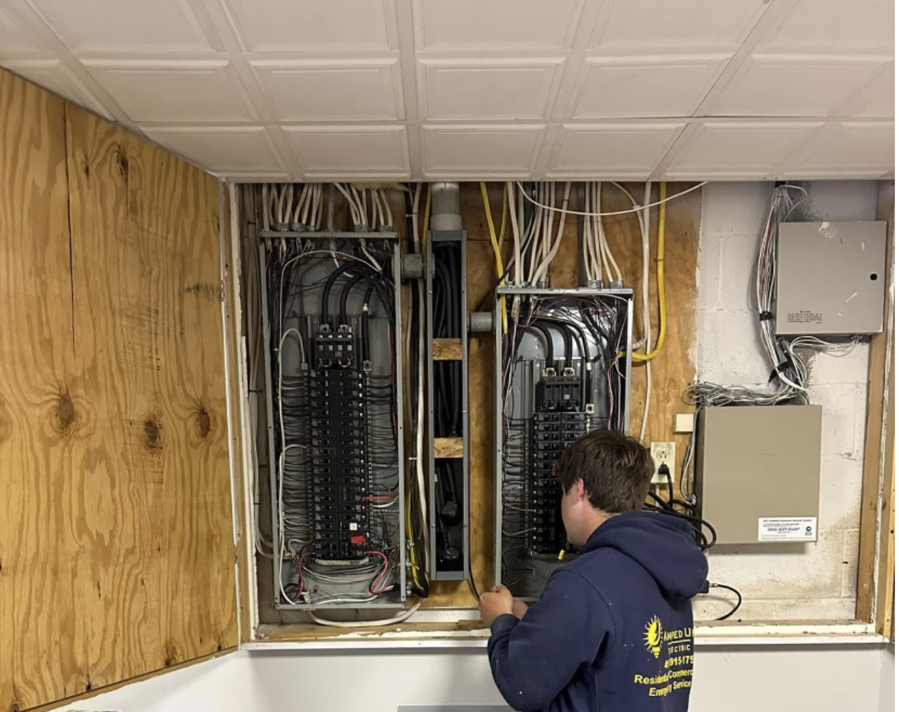 A technician working on electrical panels inside a wall cavity with various wires and electrical components.
