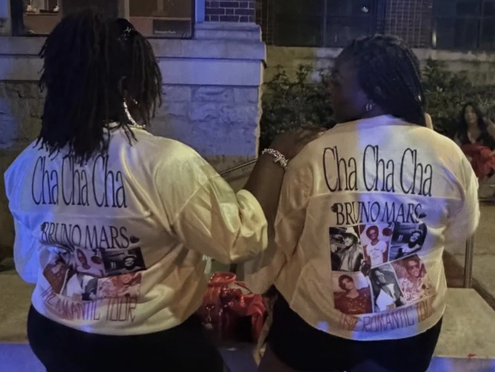 Two women wearing matching Cha Cha Cha Bruno Mars tribute jackets at an evening event.