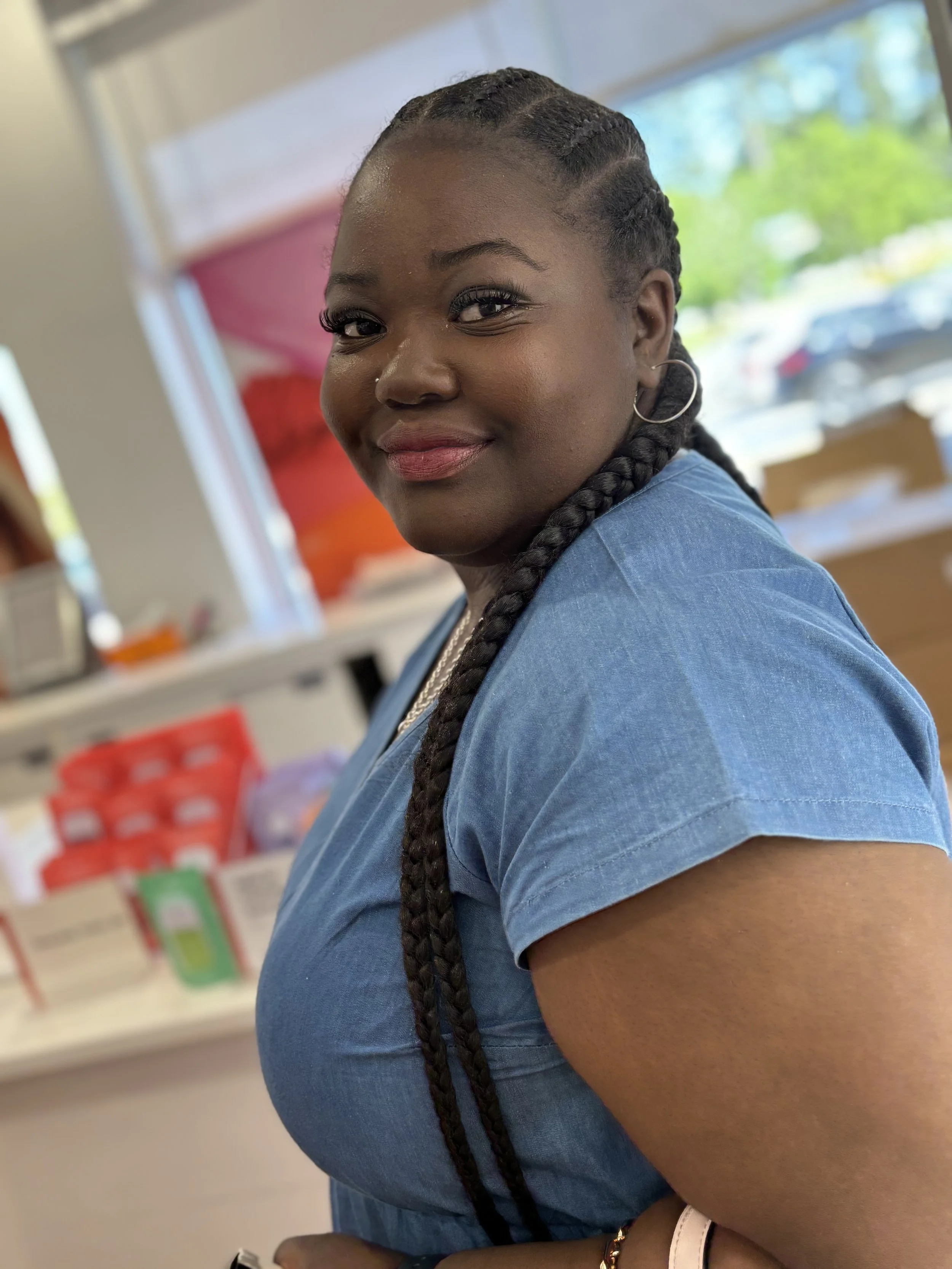 Close-up portrait of a smiling Black woman with braided hair, hoop earrings, and a blue shirt indoors.