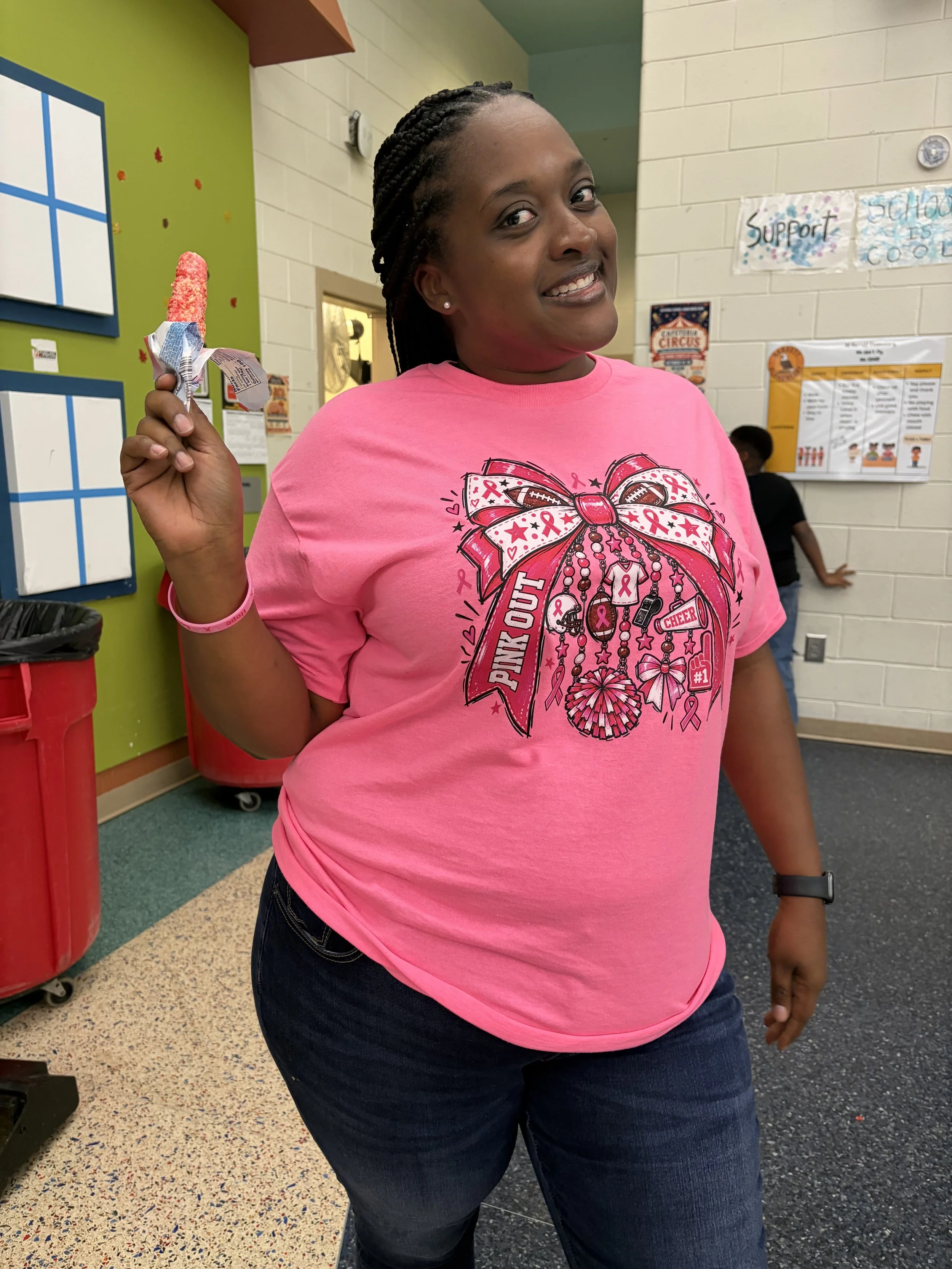 Smiling woman with braided hair holding a red frozen treat in a school hallway