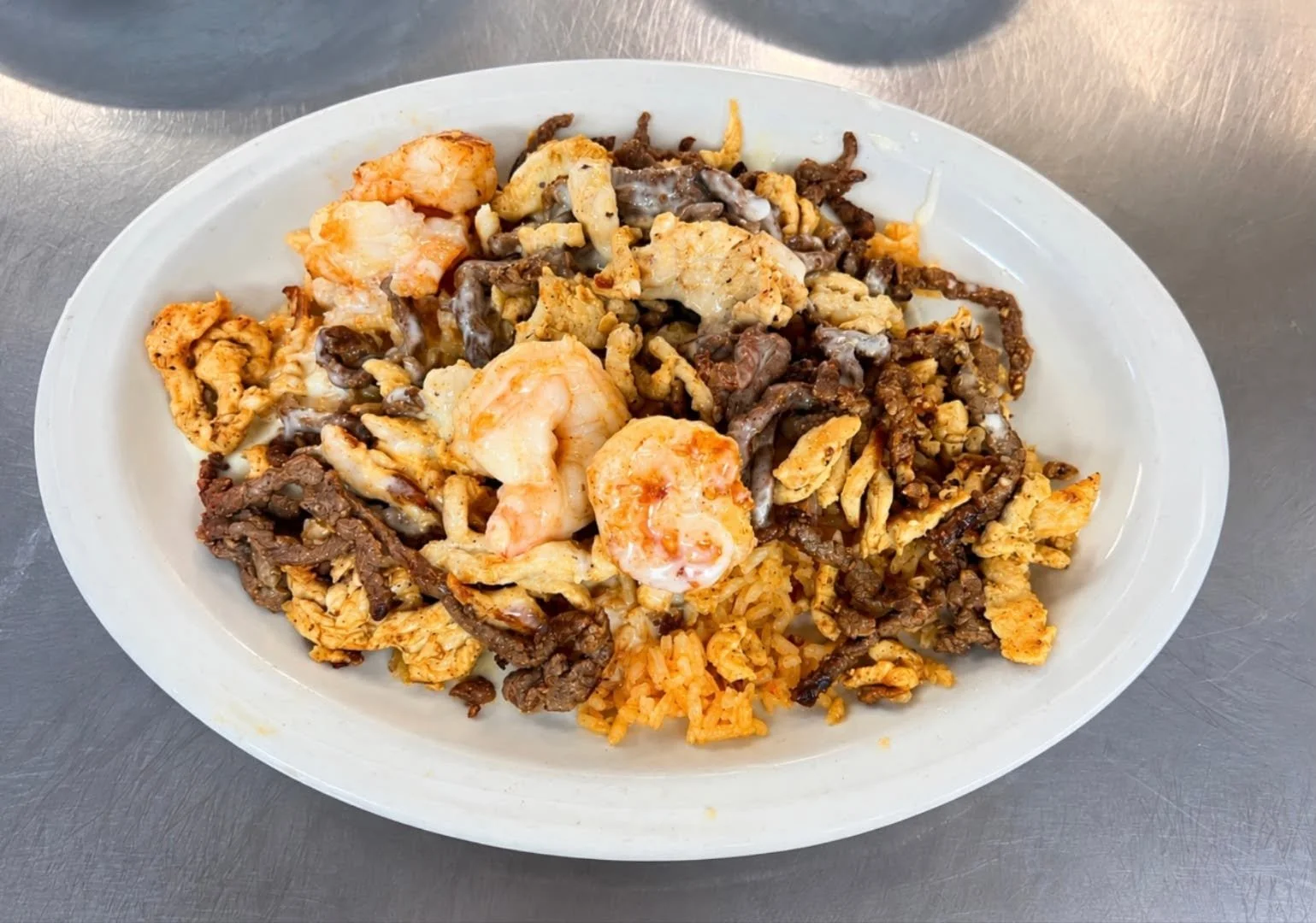 Plate of Mexican dish with rice, shrimp, beef, chicken, and grilled meat.