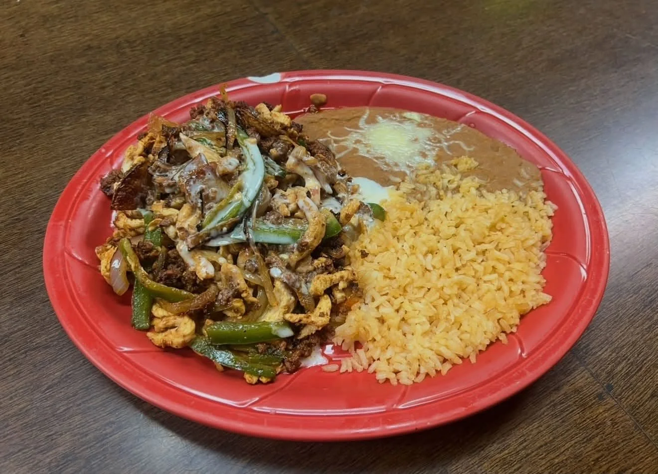 Fried rice, stir-fried beef with vegetables, and a fried egg served on a red plastic plate on a wooden table.