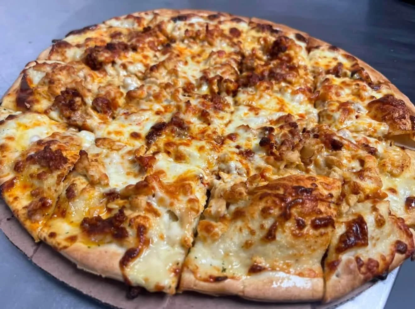A freshly baked pizza topped with cheese and meat, sliced into pieces on a dark surface.