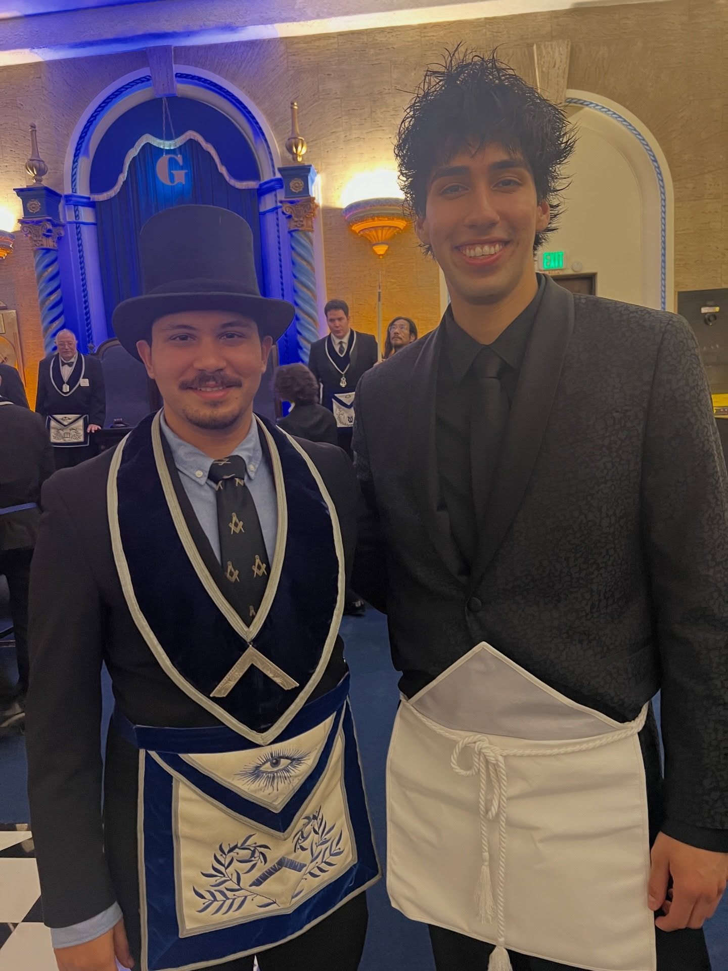 Cesar, in a white lambskin apron, poses with a man in a top hat and blue Masonic regalia in the lodge room. 