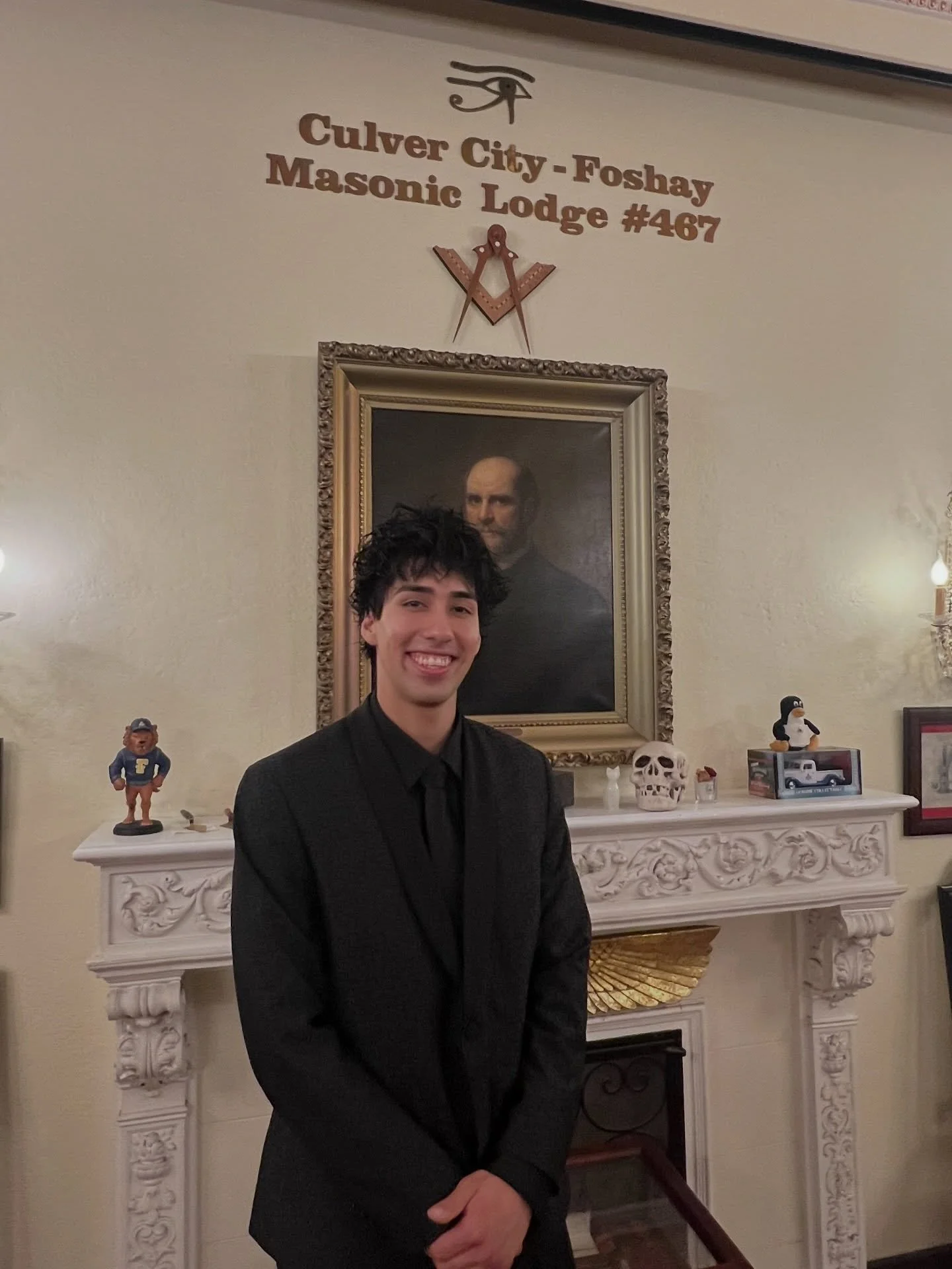 Cesar, smiling in a black suit, stands before the fireplace under the Culver City-Foshay Masonic Lodge #467 sign.