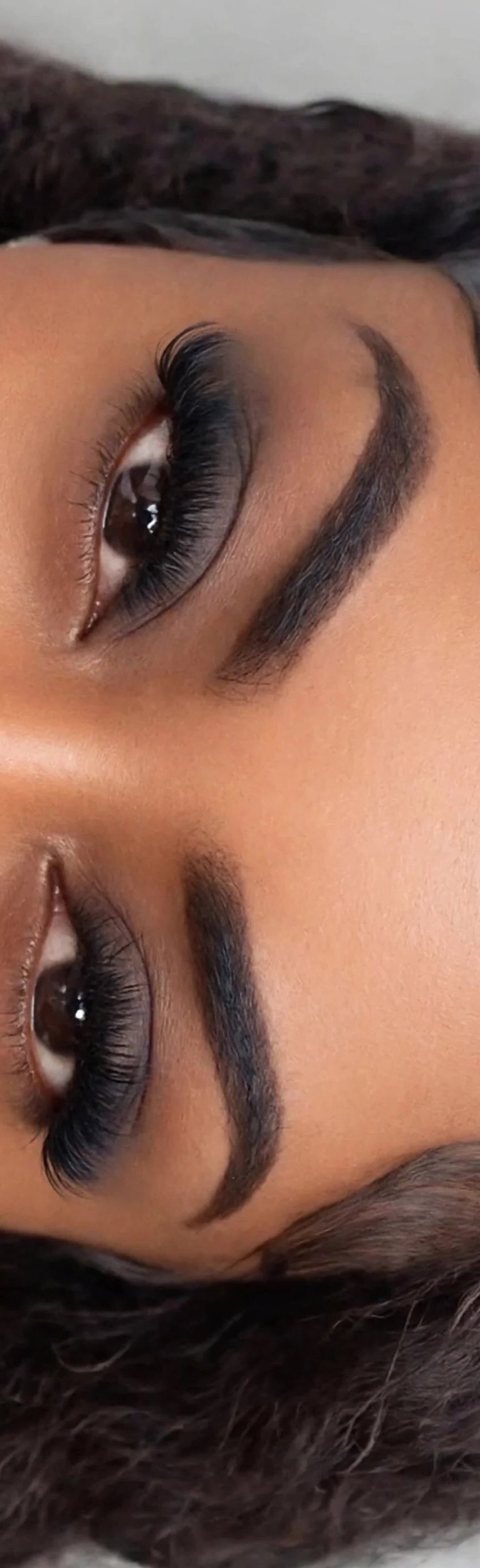 Close-up portrait of a woman with long eyelashes, defined eyebrows, and brown eyes.