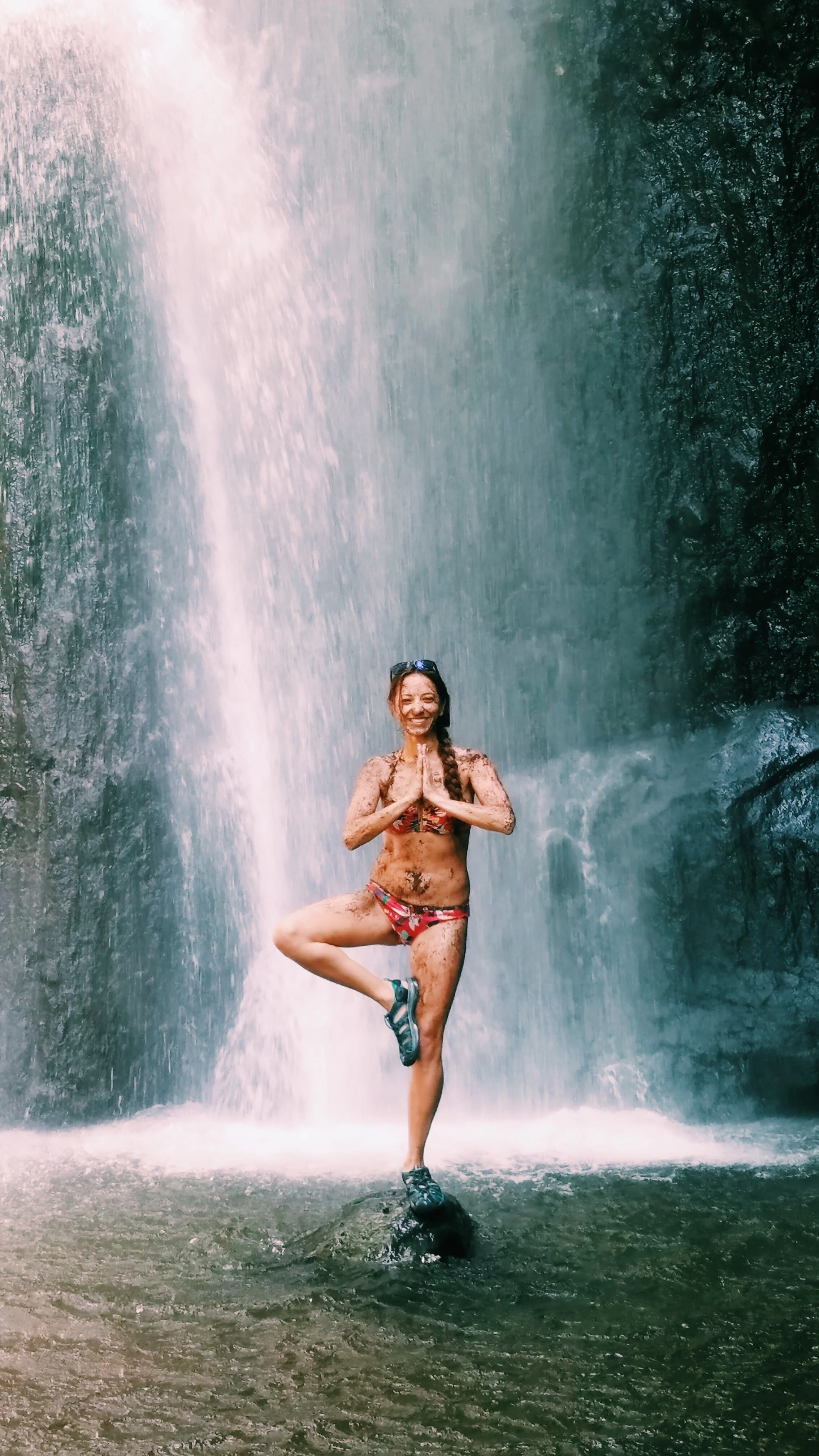 Melanie Boling practicing tree pose in a colorful bikini beneath a waterfall in North Bali, Indonesia.