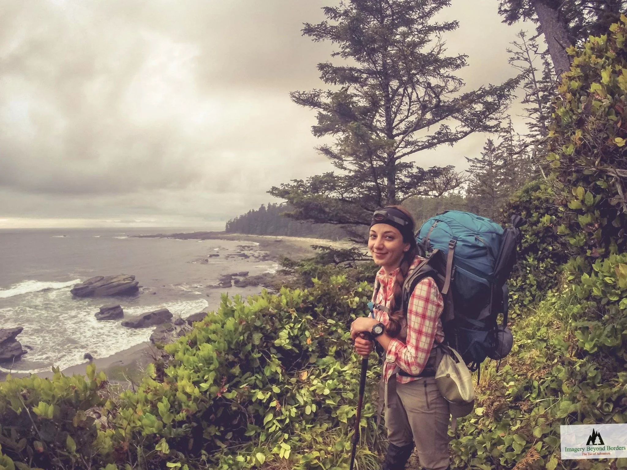 Melanie Boling with a large backpack trekking along a lush West Coastal Trail overlooking a rocky ocean shoreline in British Columbia.