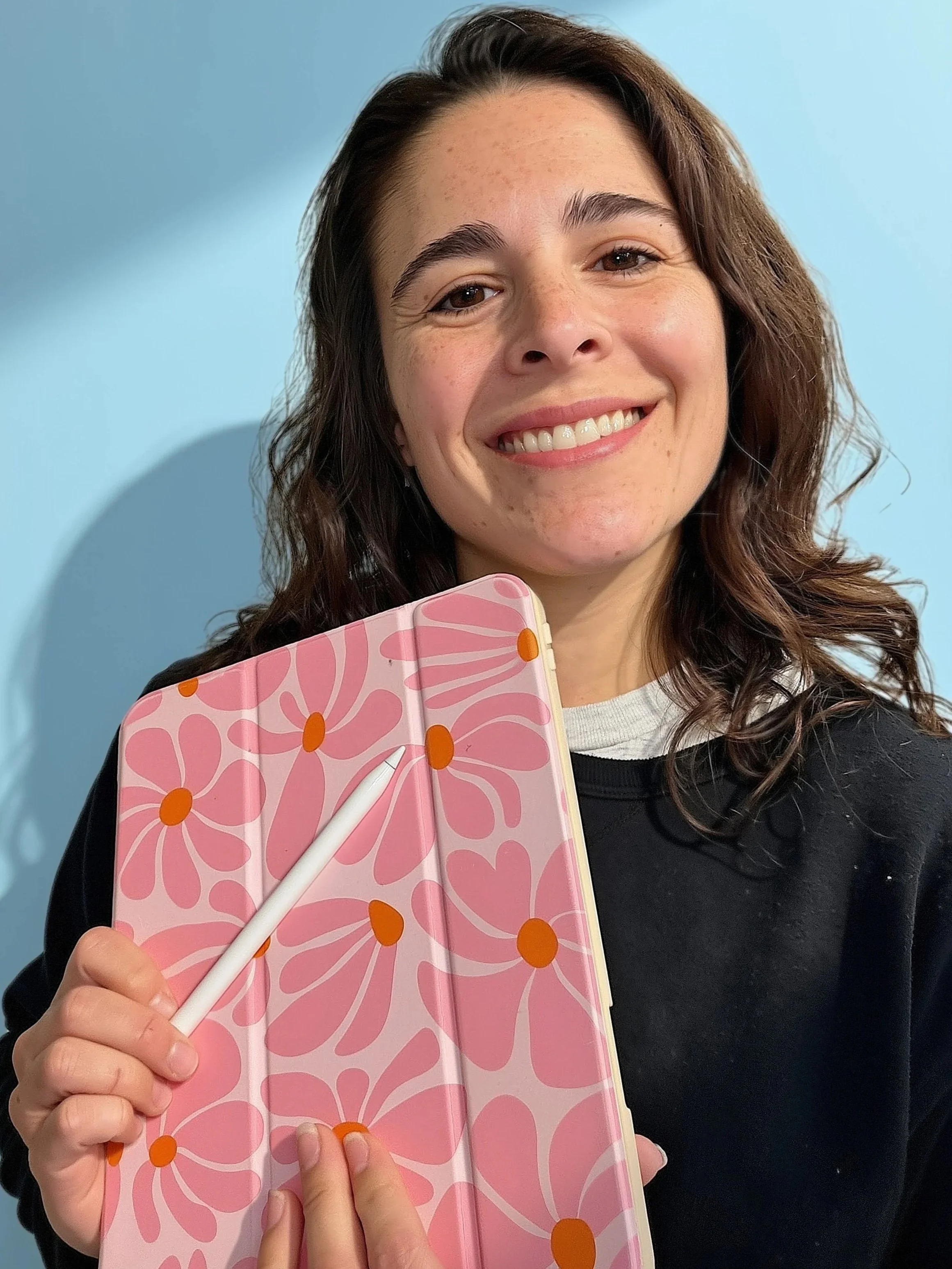 Smiling woman holding a pink floral notebook and white pen against a blue background
