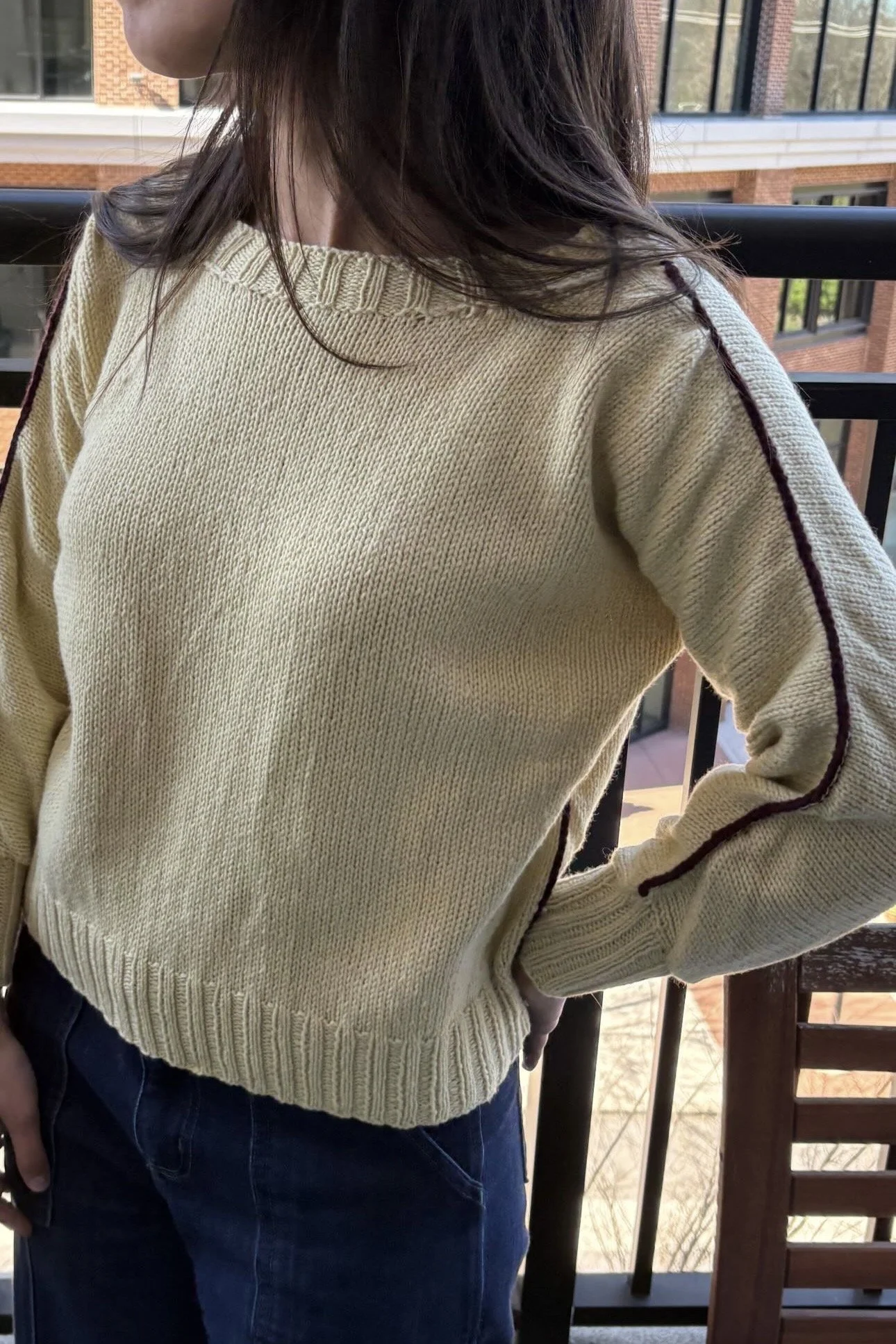 Person wearing a cream knit sweater and dark jeans on a balcony