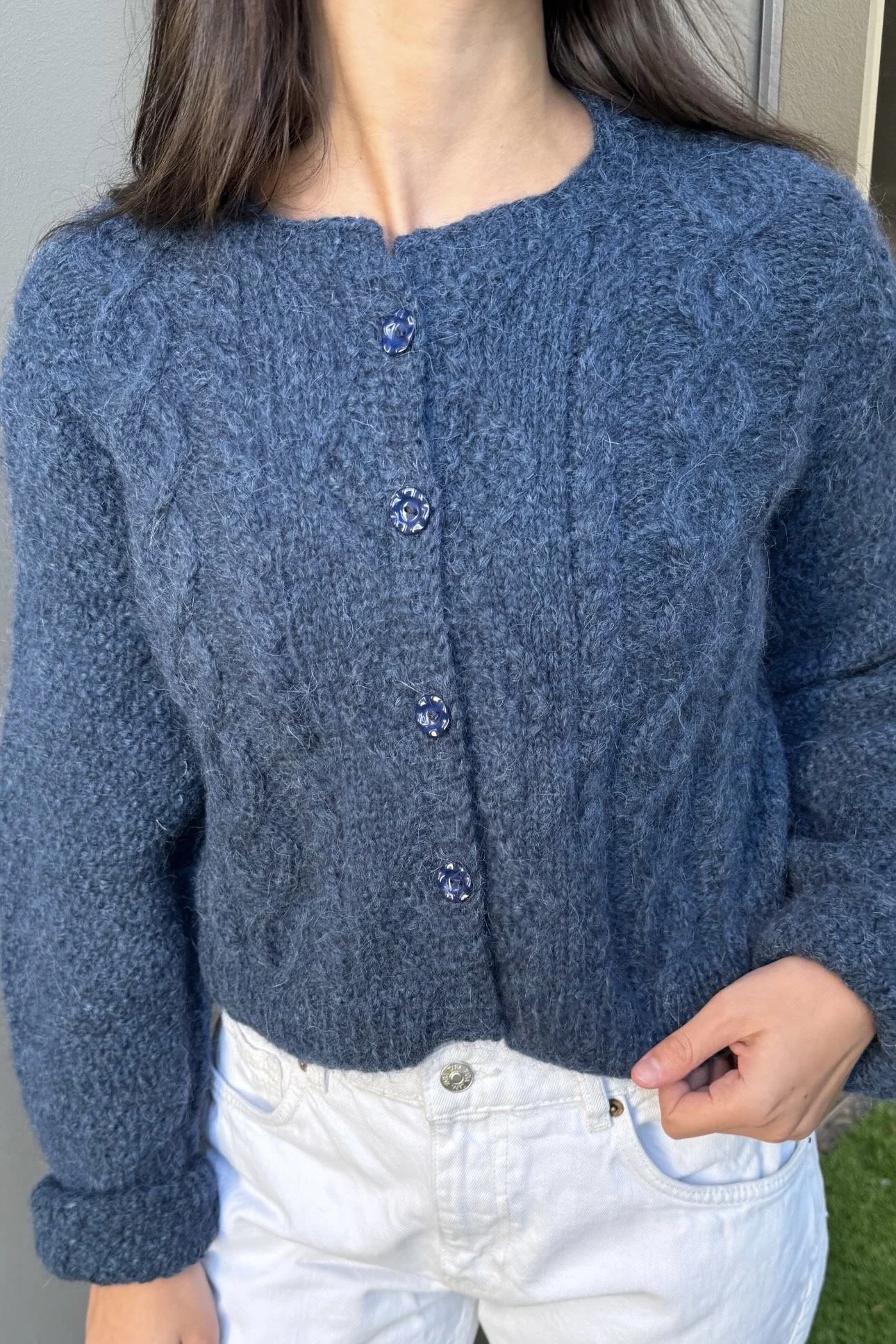 Close-up of a woman wearing a fuzzy blue button-front knit cardigan with white jeans