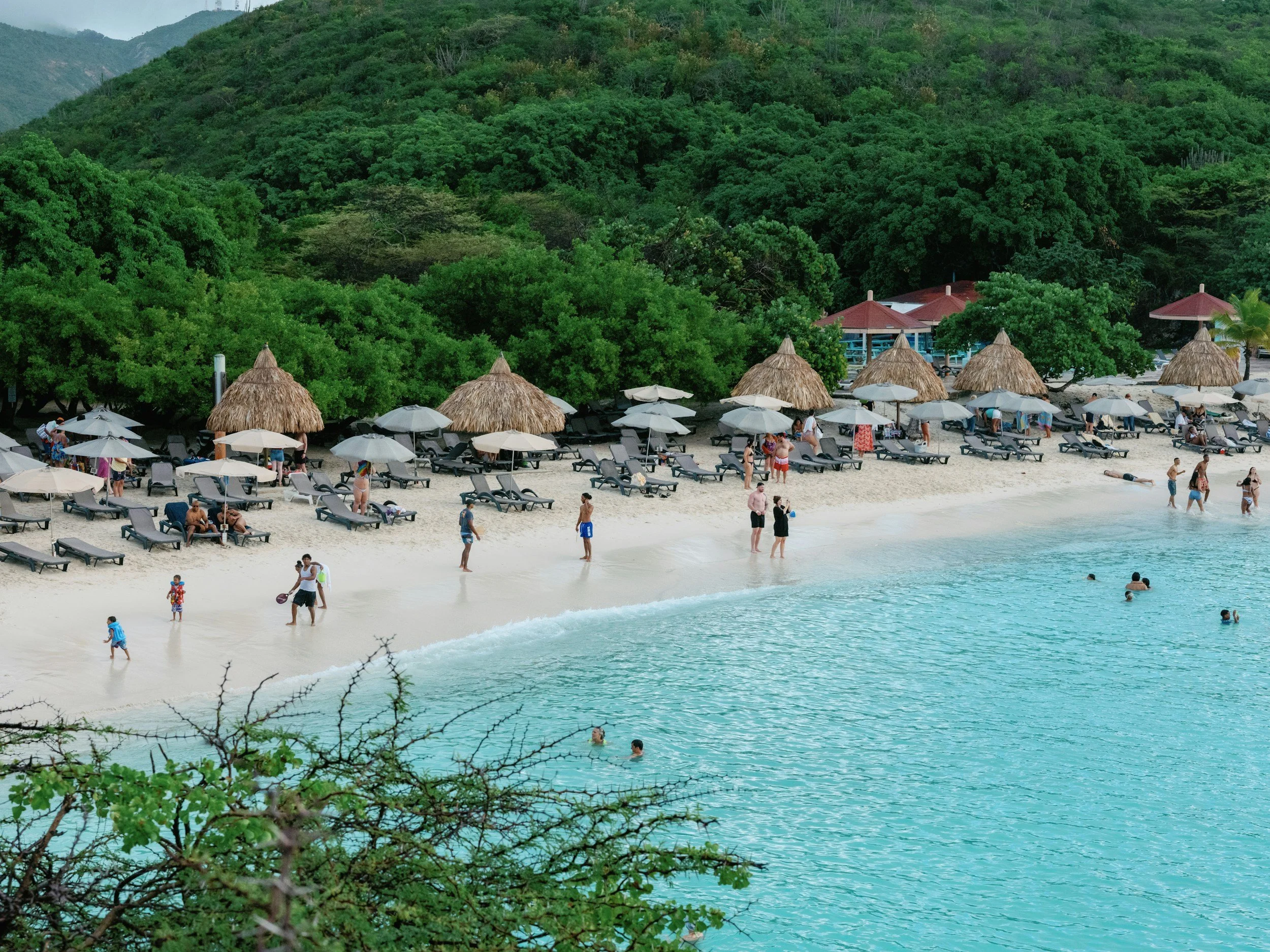 A small cove beach with thatched umbrellas, turquoise water and green hills
