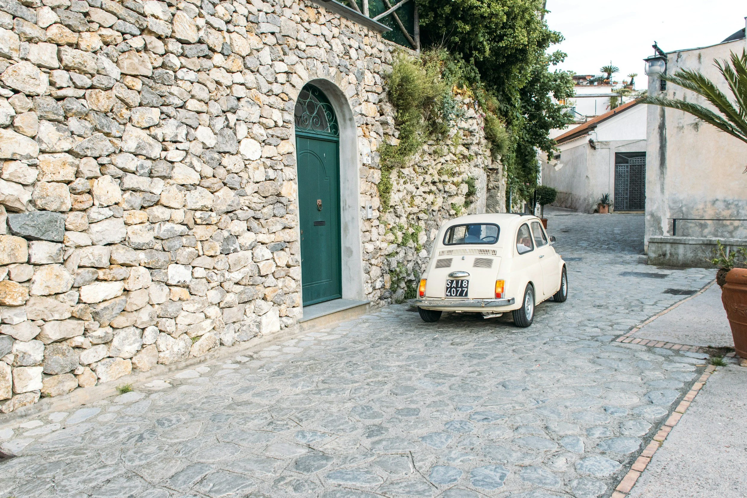 A small vintage car parked on a narrow cobblestone lane between stone walls