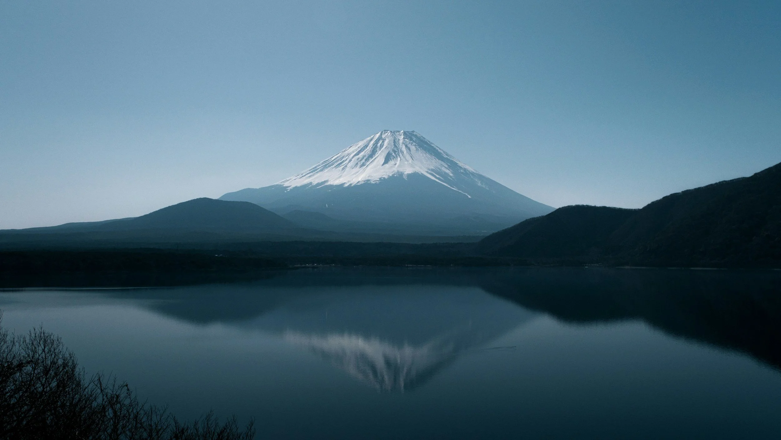 Snow-capped Mount Fuji reflected in a calm lake at dusk