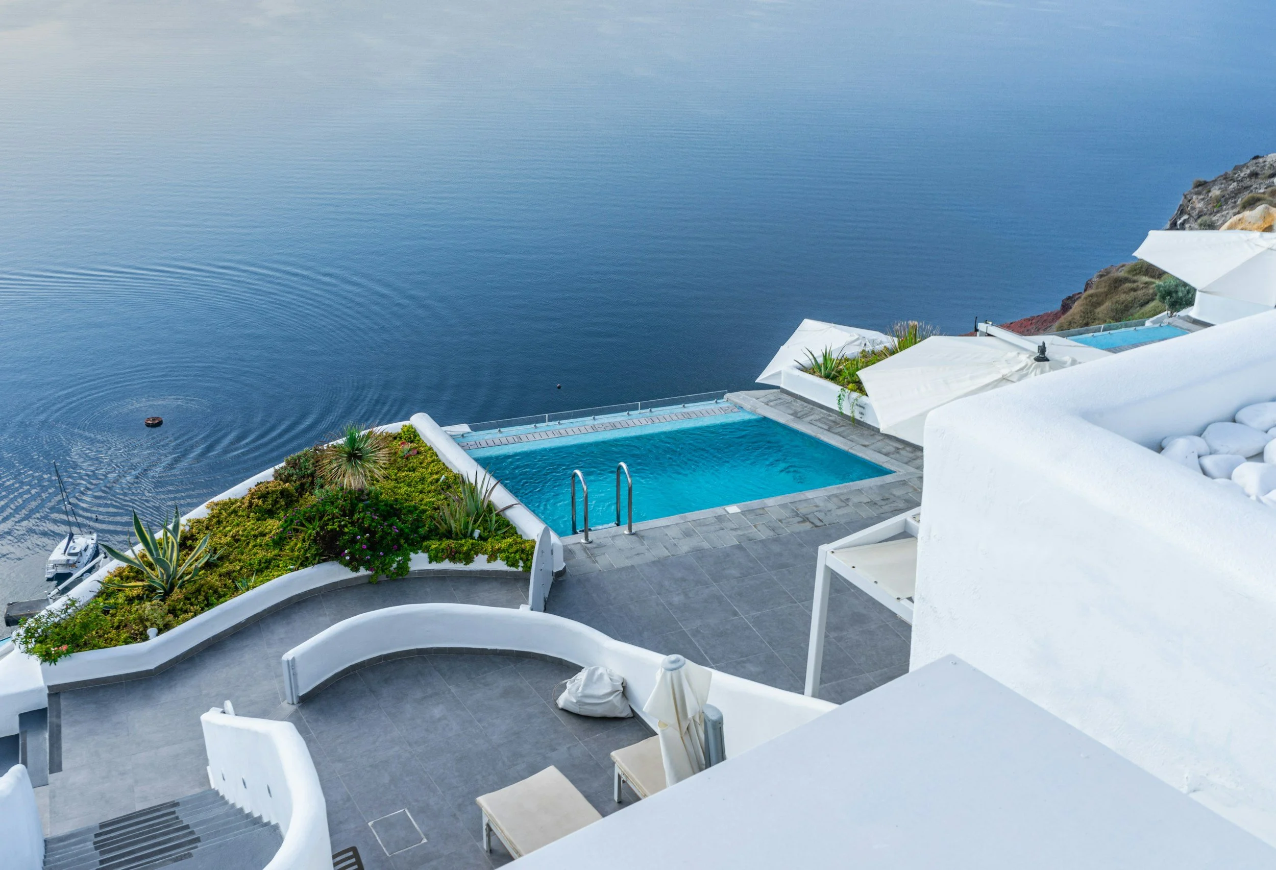 A whitewashed cliffside hotel with a blue infinity pool overlooking the Aegean Sea in Greece