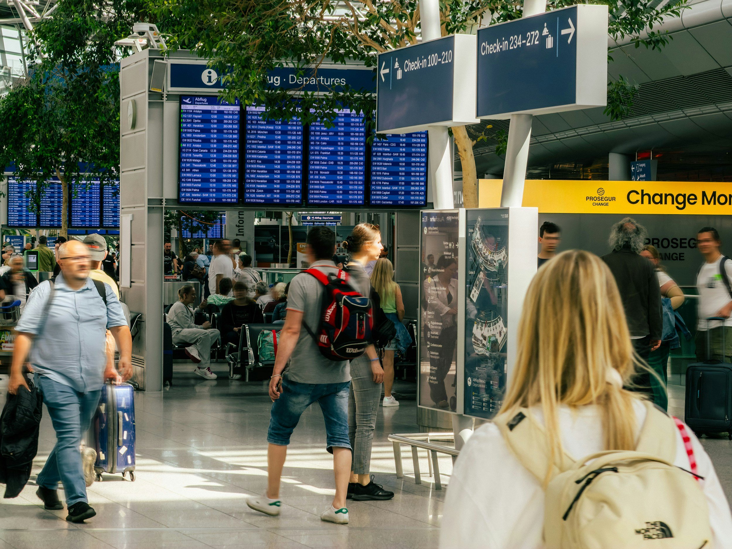 Travelers with backpacks walking beneath flight departure boards in a busy airport terminal