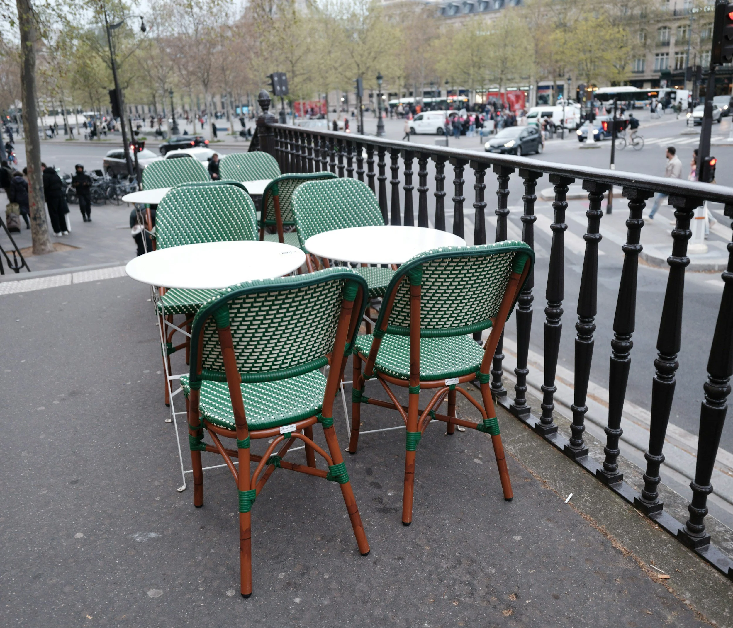 Green woven bistro chairs and small round tables on a Paris café terrace beside a tree-lined street