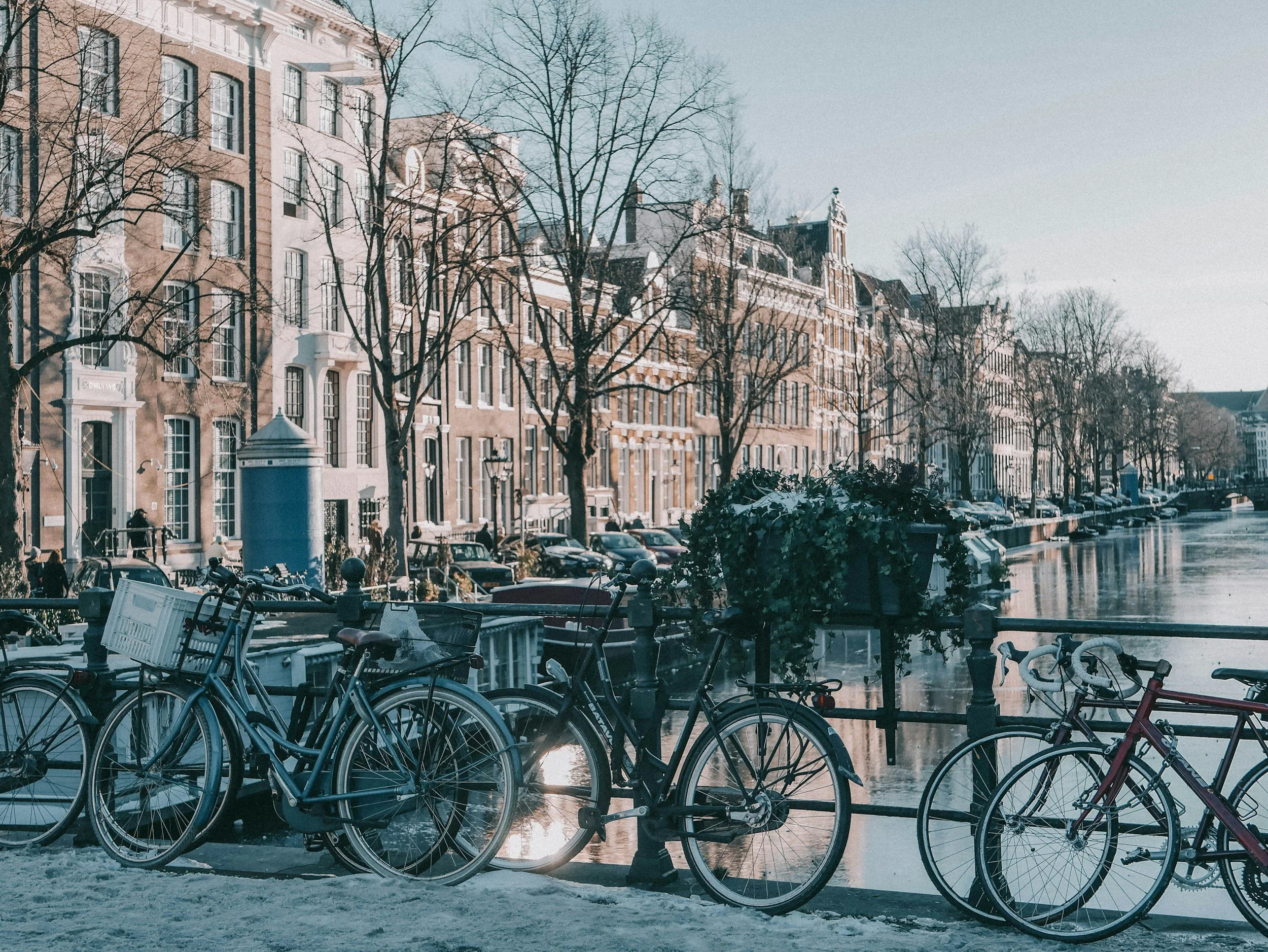 Rows of bicycles parked along a canal railing in front of tall, narrow Amsterdam canal houses