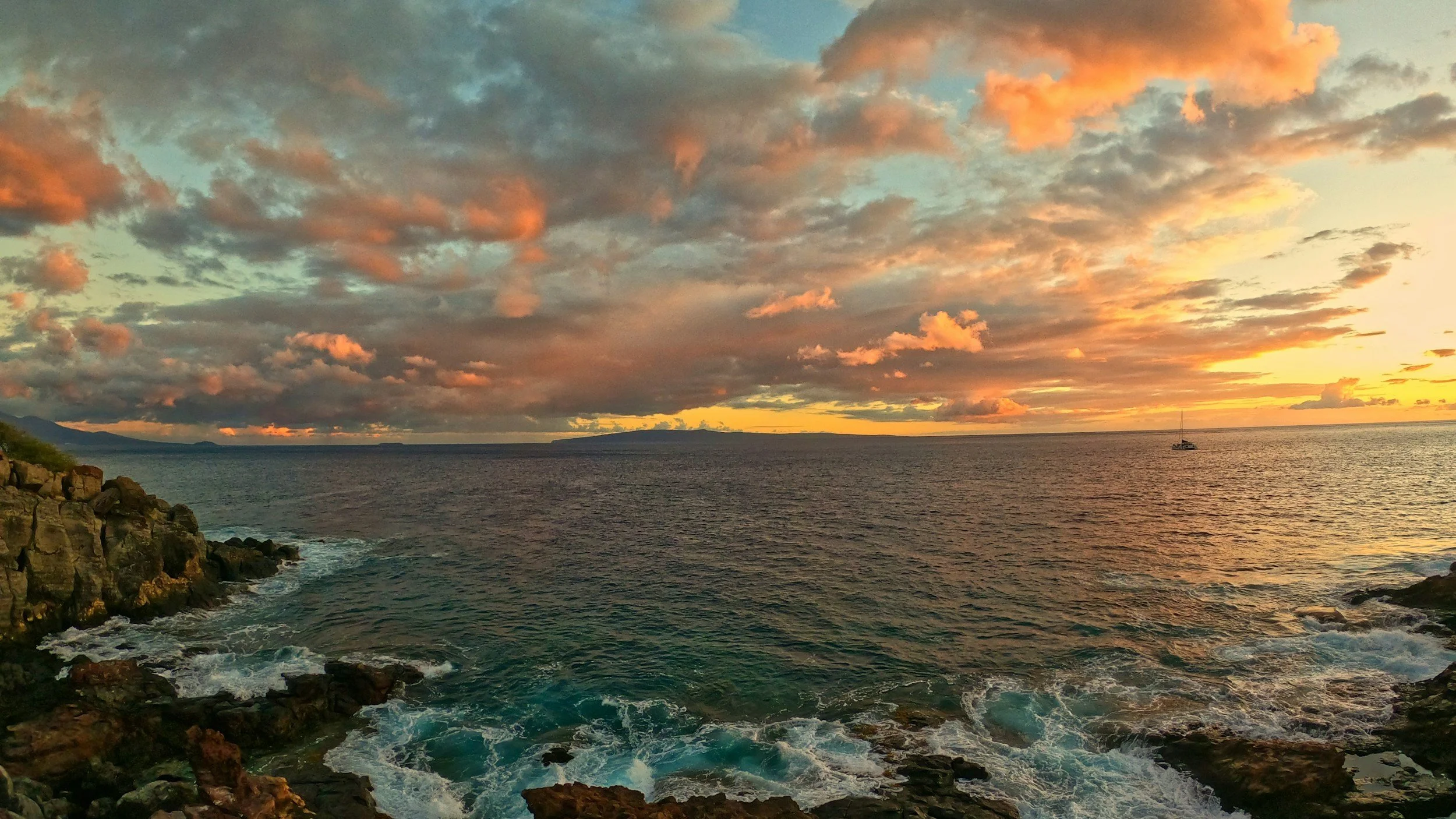 A fiery orange sunset over a rocky shoreline and the open sea